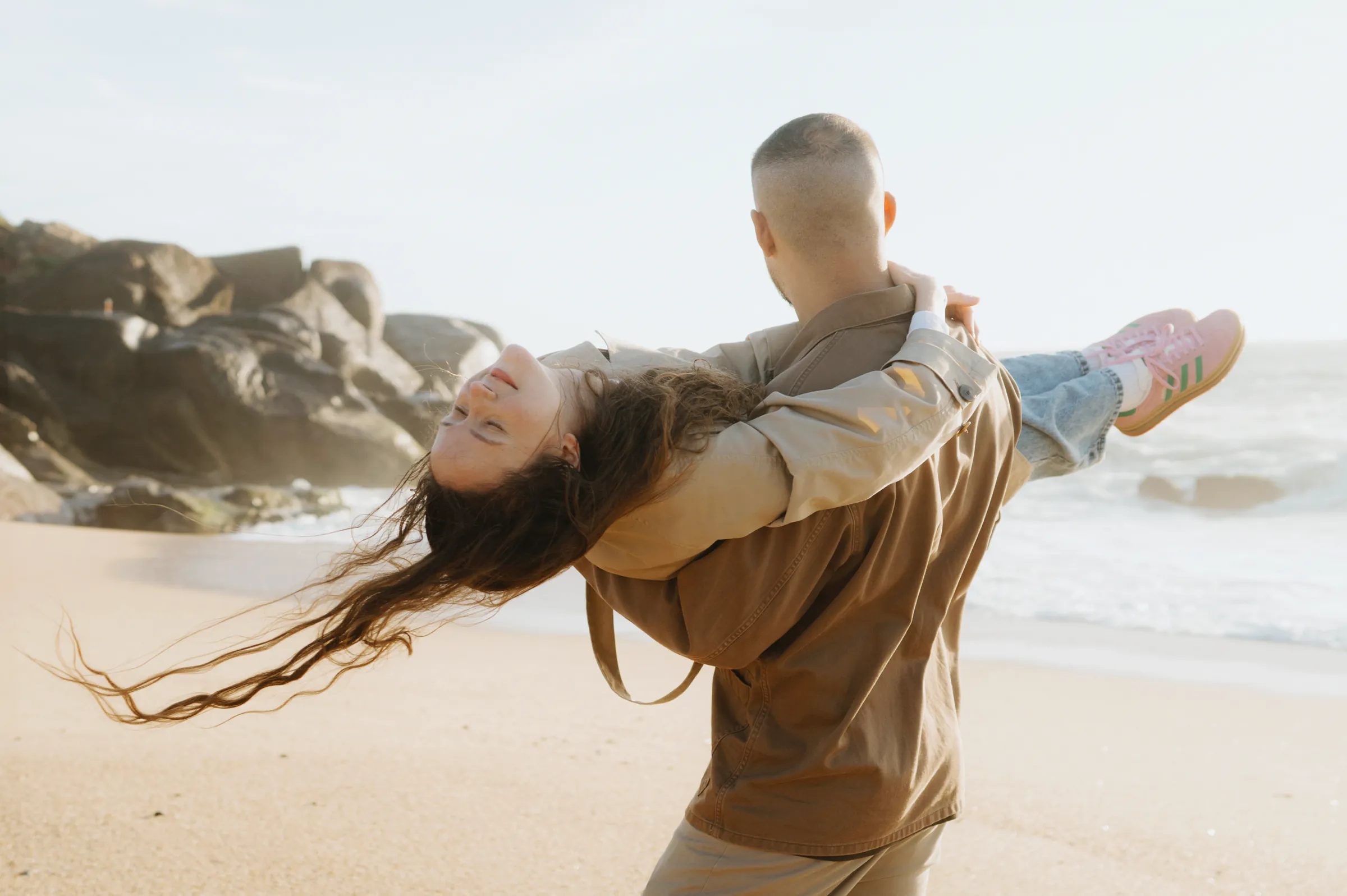 Couple during a seaside session, one carrying the other along the beach in soft light.