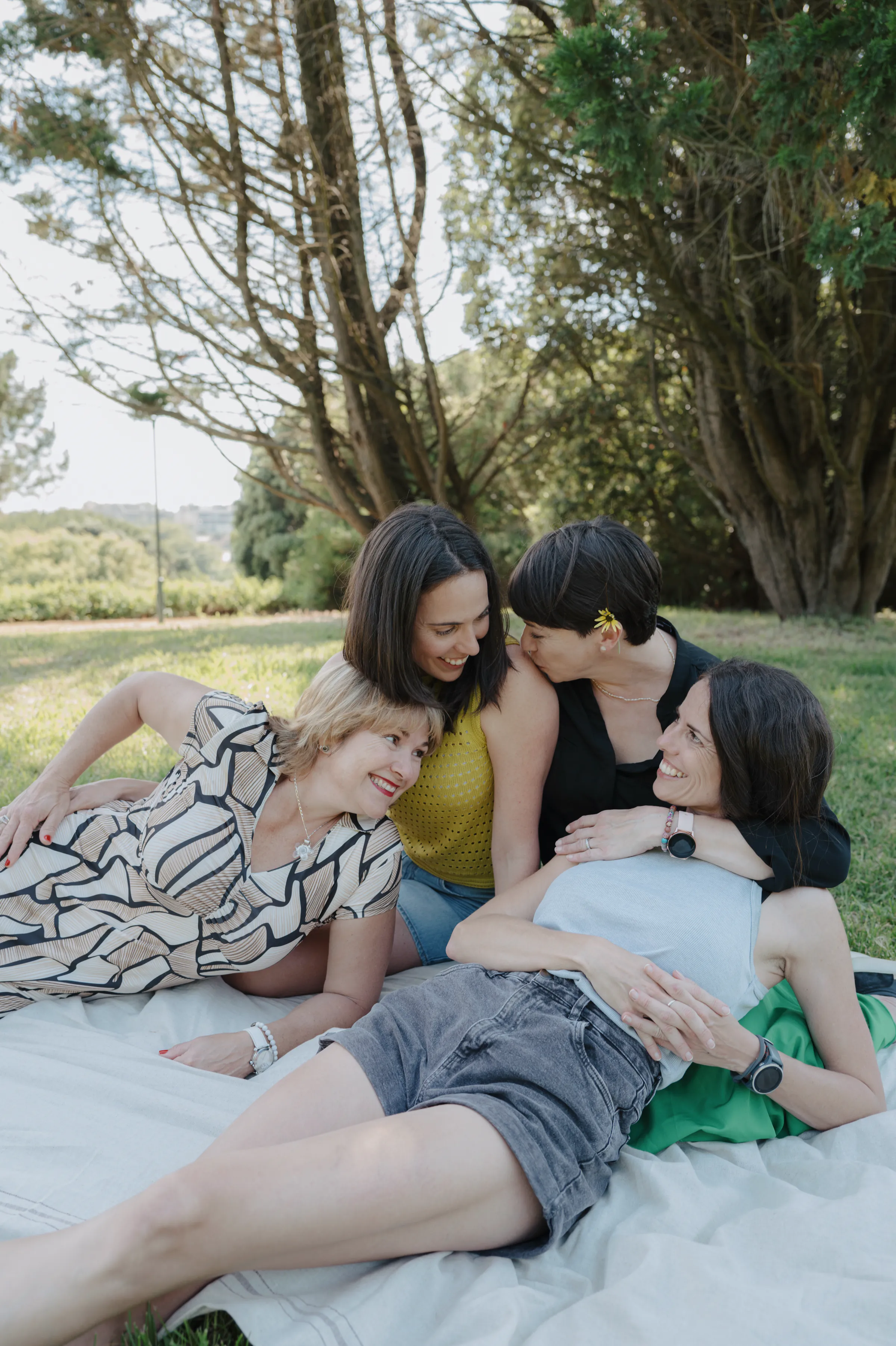 Four adults reclining on a blanket during an outdoor session in soft light under trees.