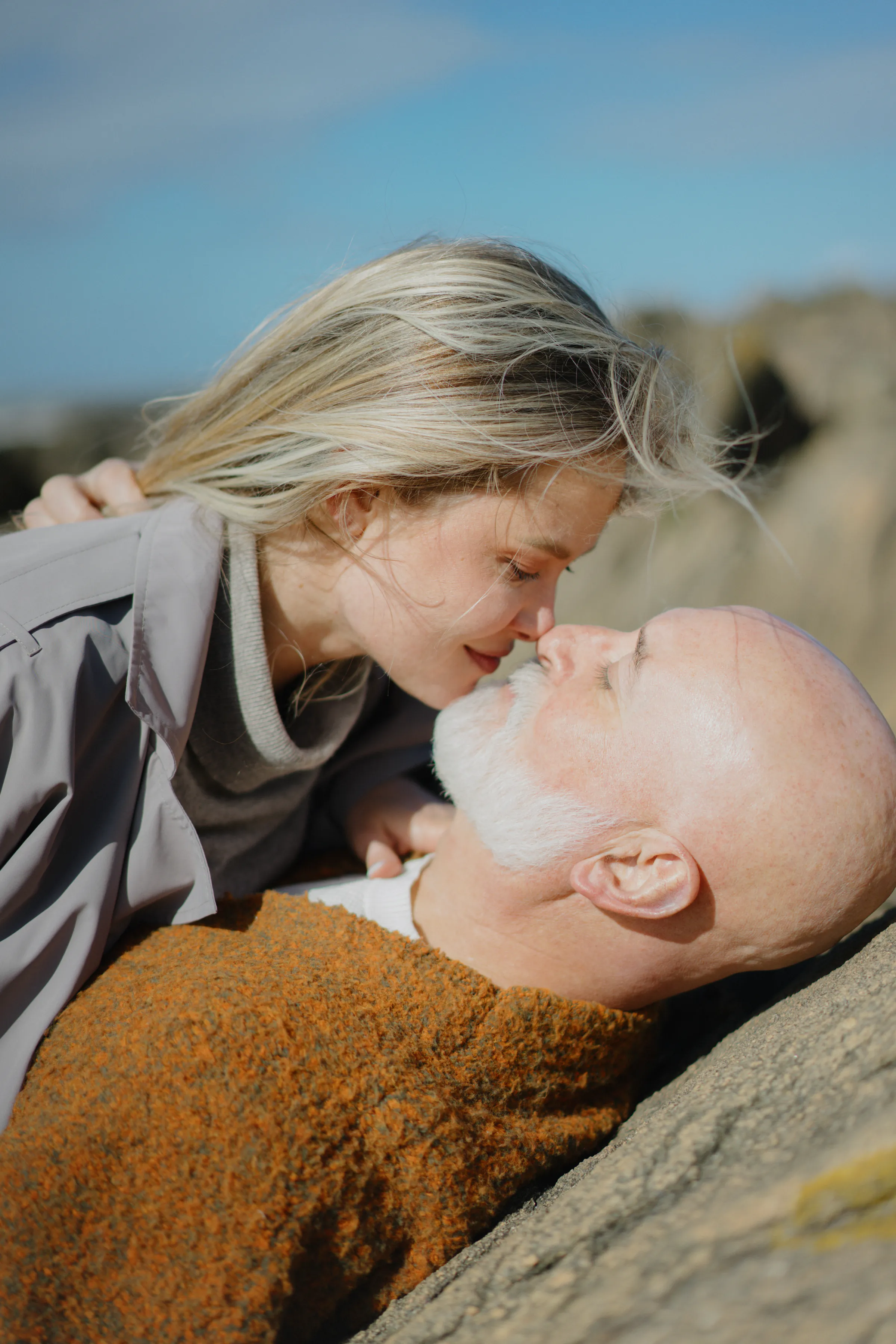 Close outdoor portrait of a couple leaning together on a rock in soft light.