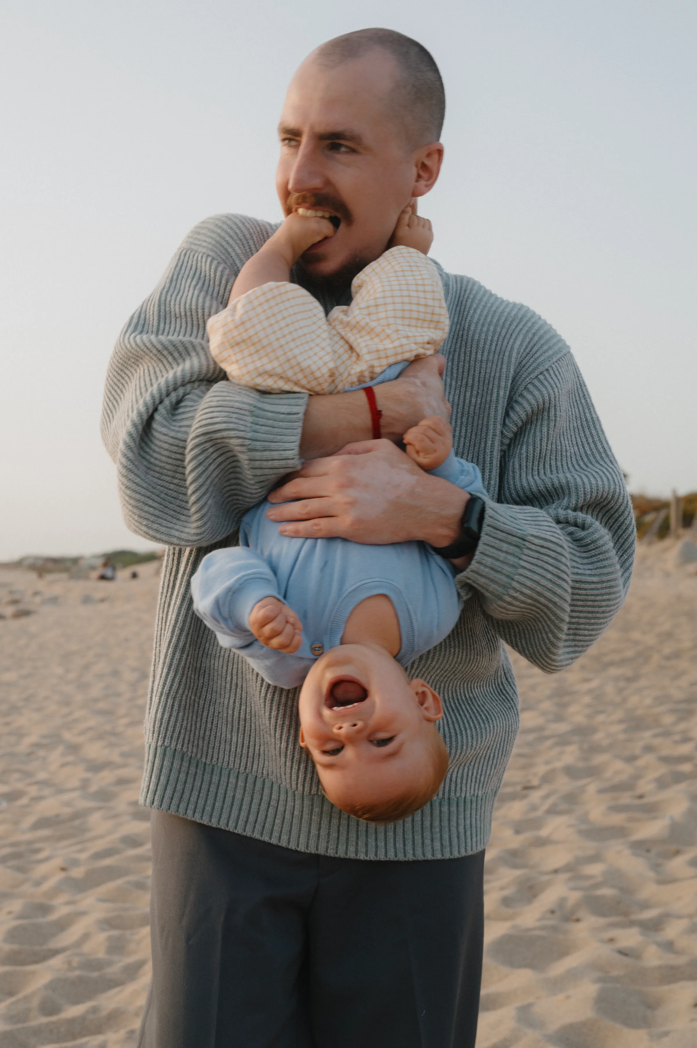 Family seaside portrait with an adult holding a baby upside down in soft light