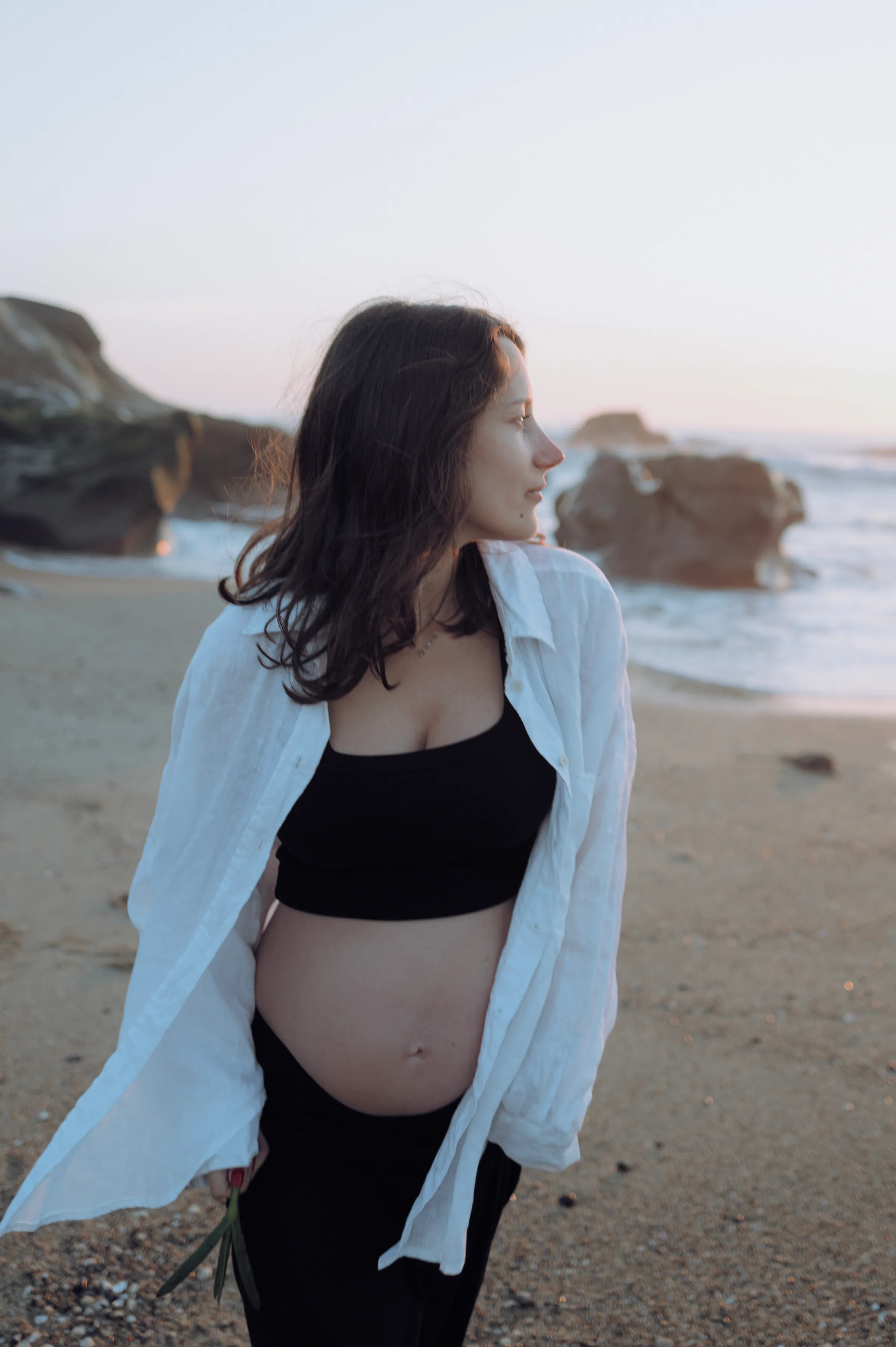 Seaside portrait of a person in a white shirt standing on a sandy beach in soft light.