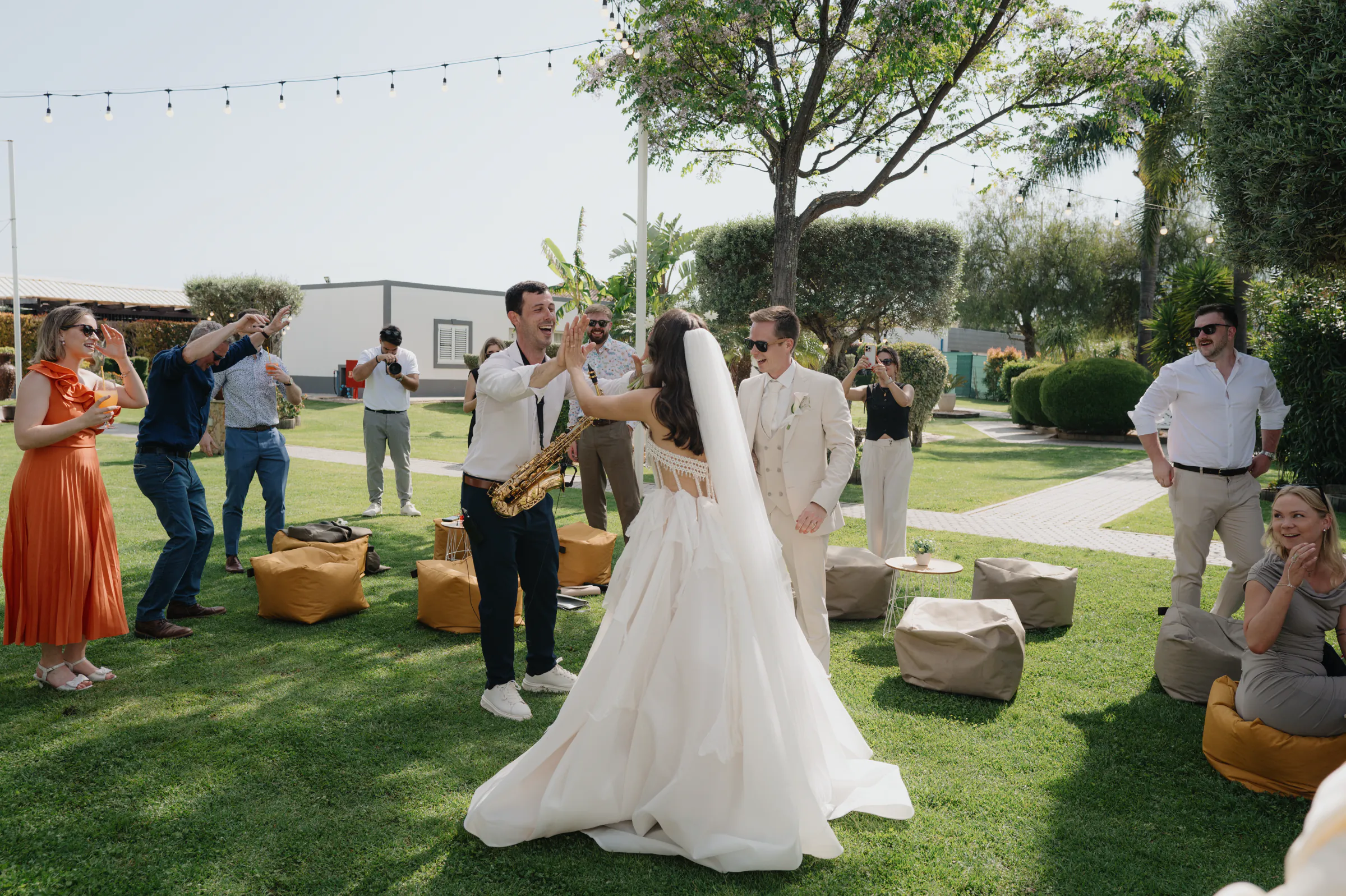 Couple dancing on a garden lawn during an outdoor wedding reception, surrounded by guests and soft daylight.