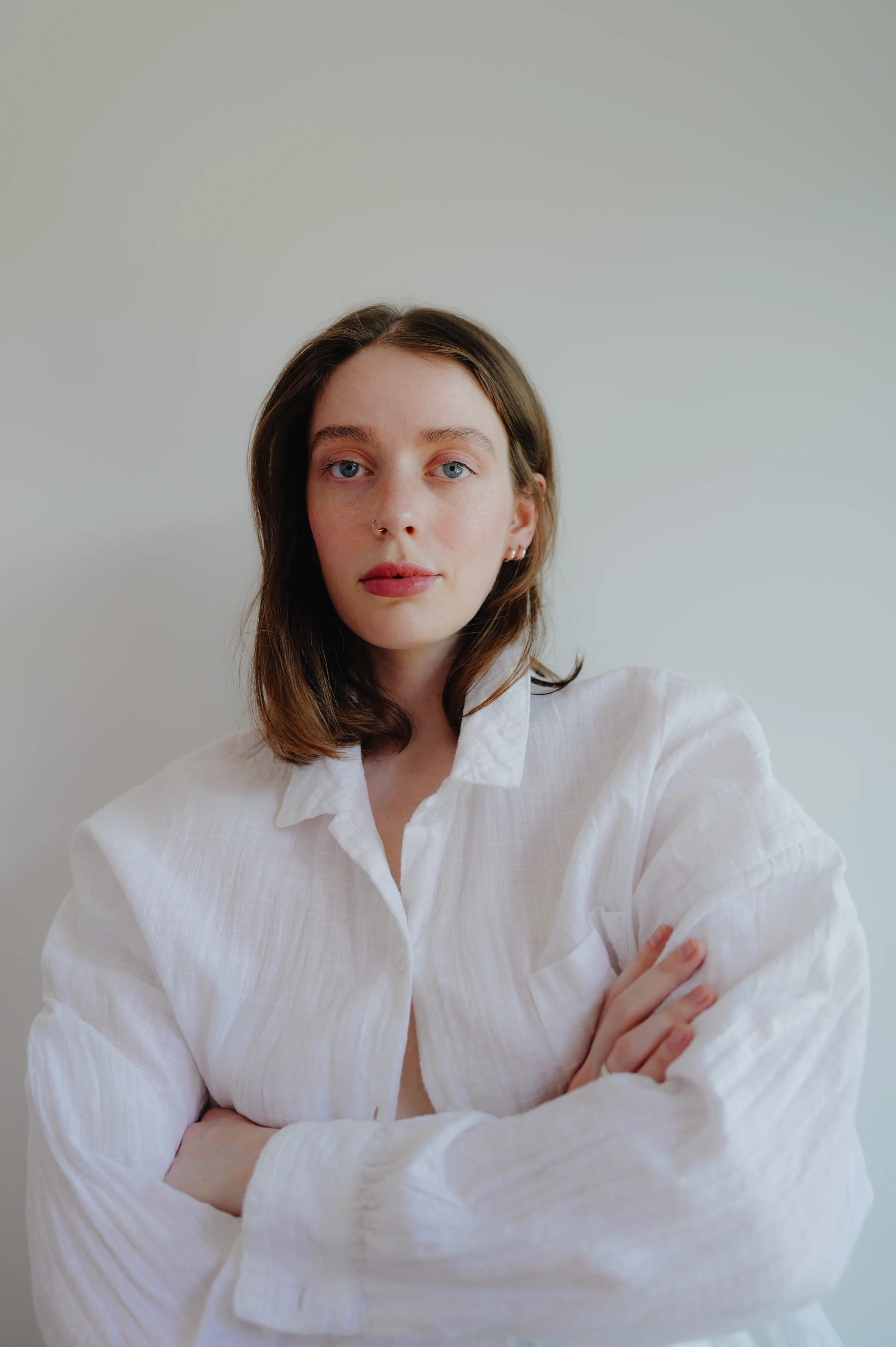 Close portrait of a person in a white shirt with crossed arms against a plain wall.
