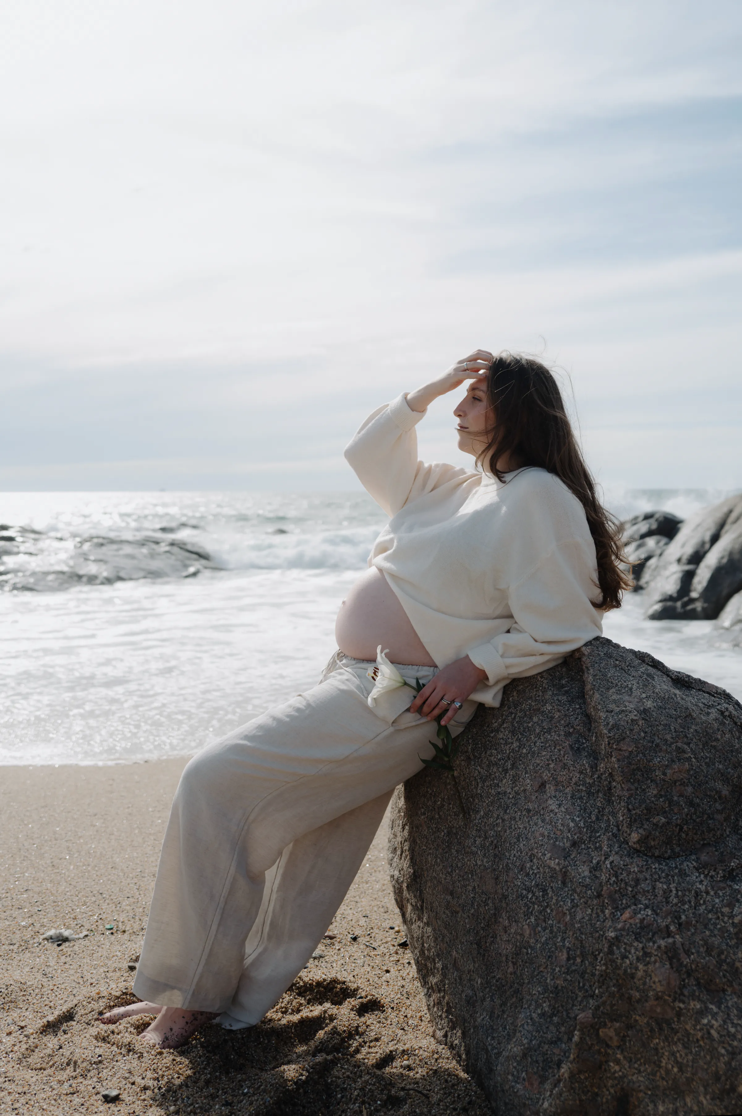 Outdoor seaside portrait of a person in white seated on a rock in soft light.