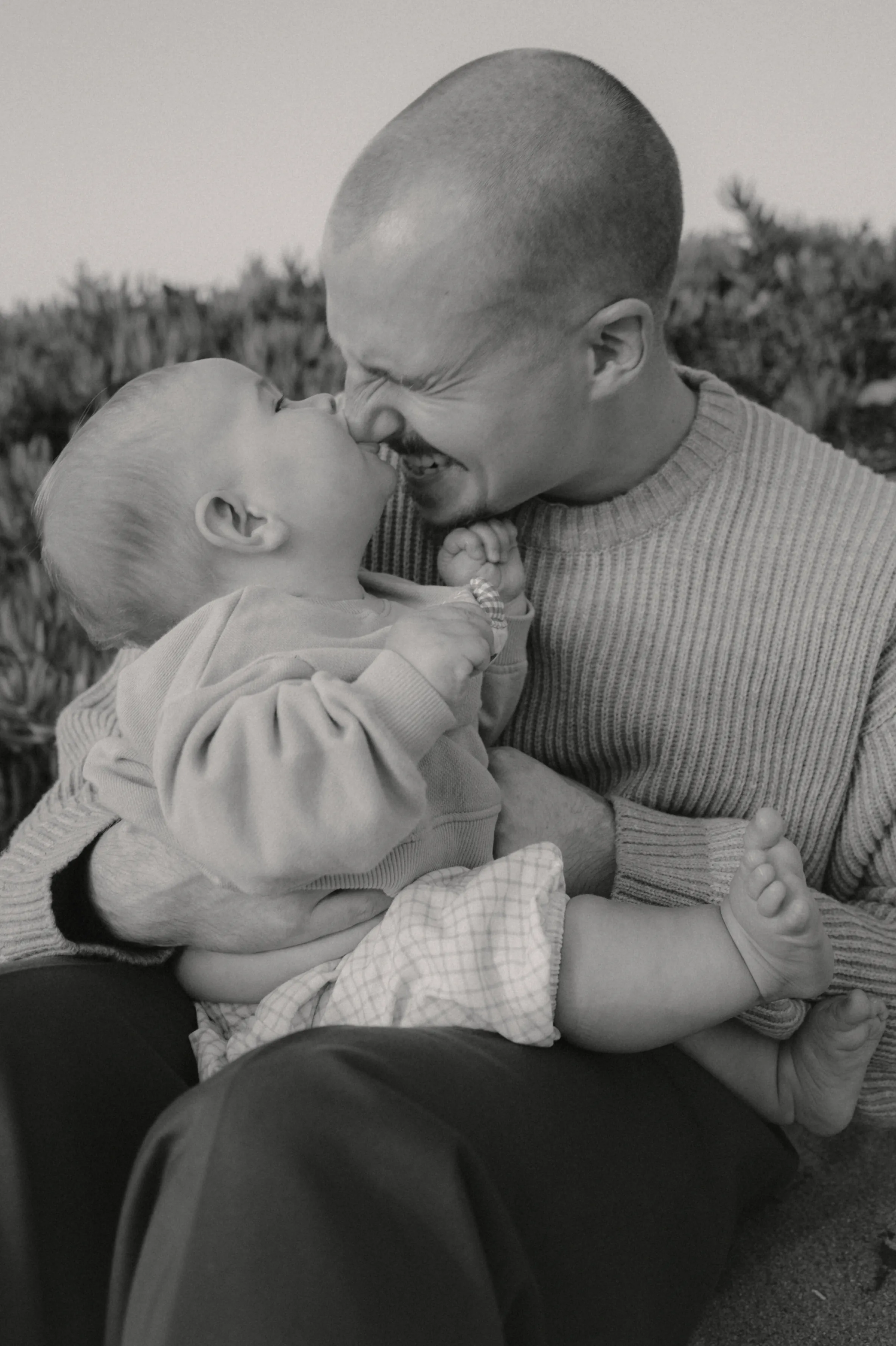 Black-and-white close portrait of an adult holding a baby during an outdoor session.