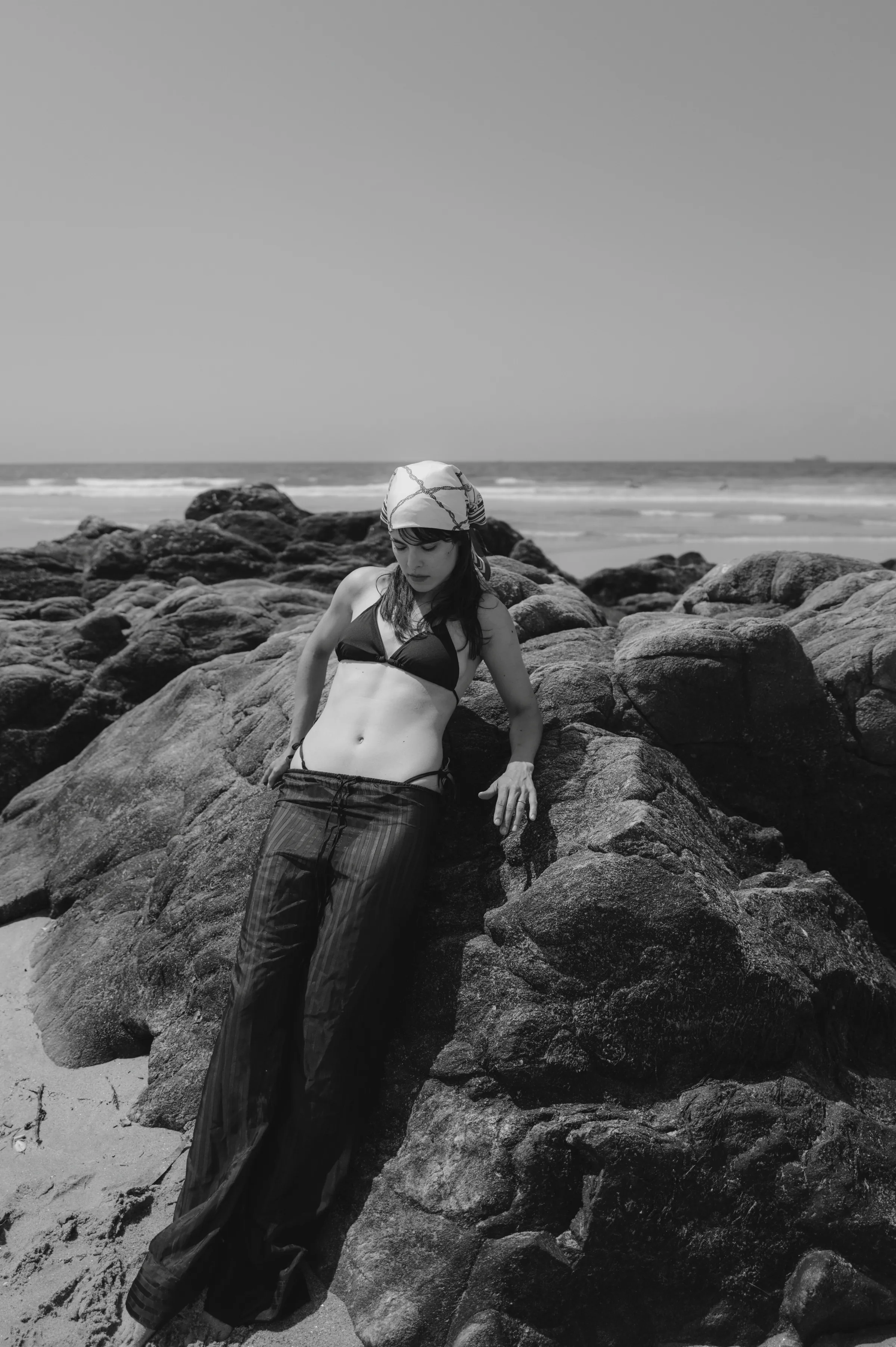 Black-and-white seaside portrait of a person leaning on rocks near the ocean.