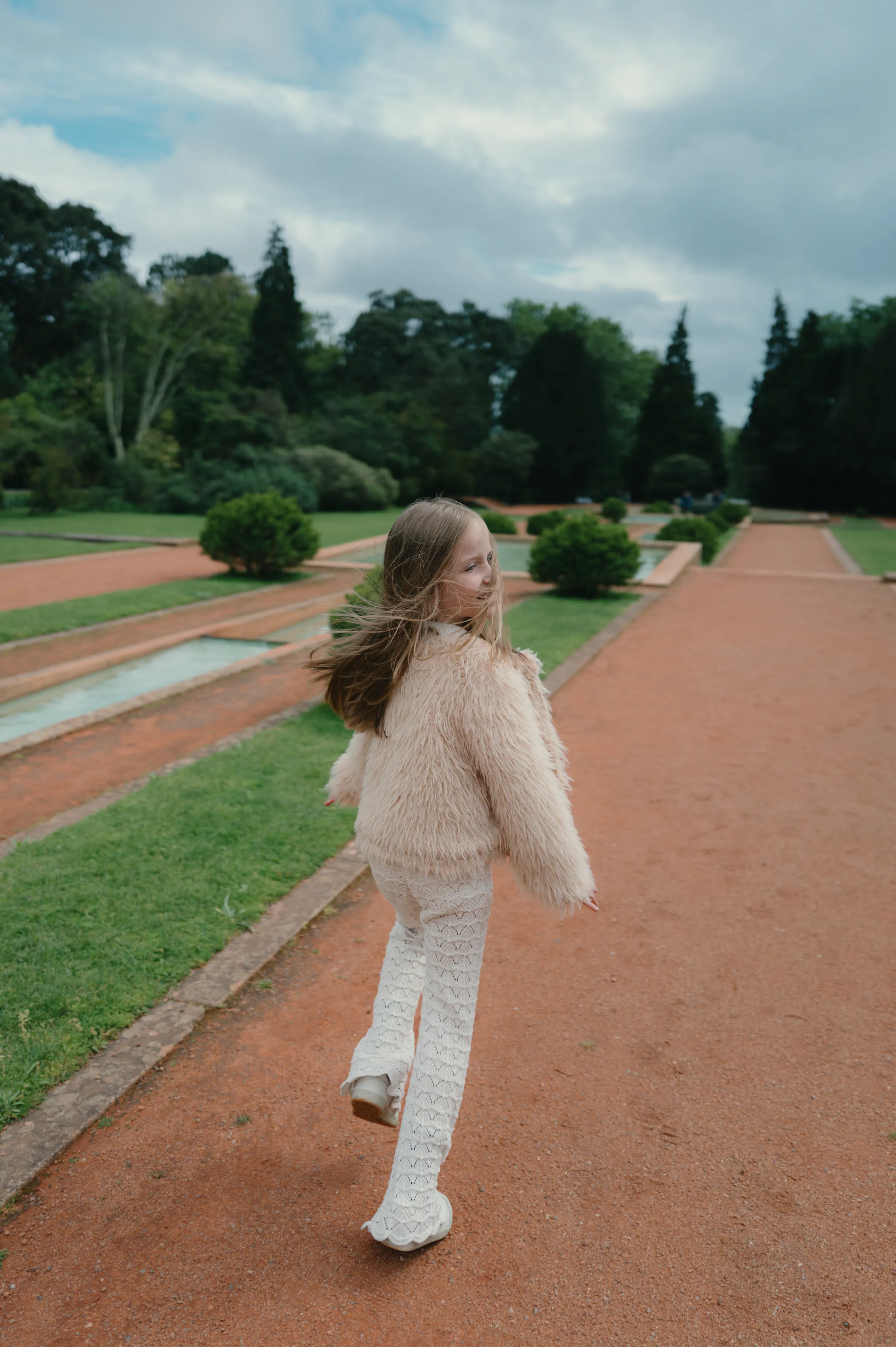 Child turning back while walking along a garden path during an outdoor session in soft cloudy light.