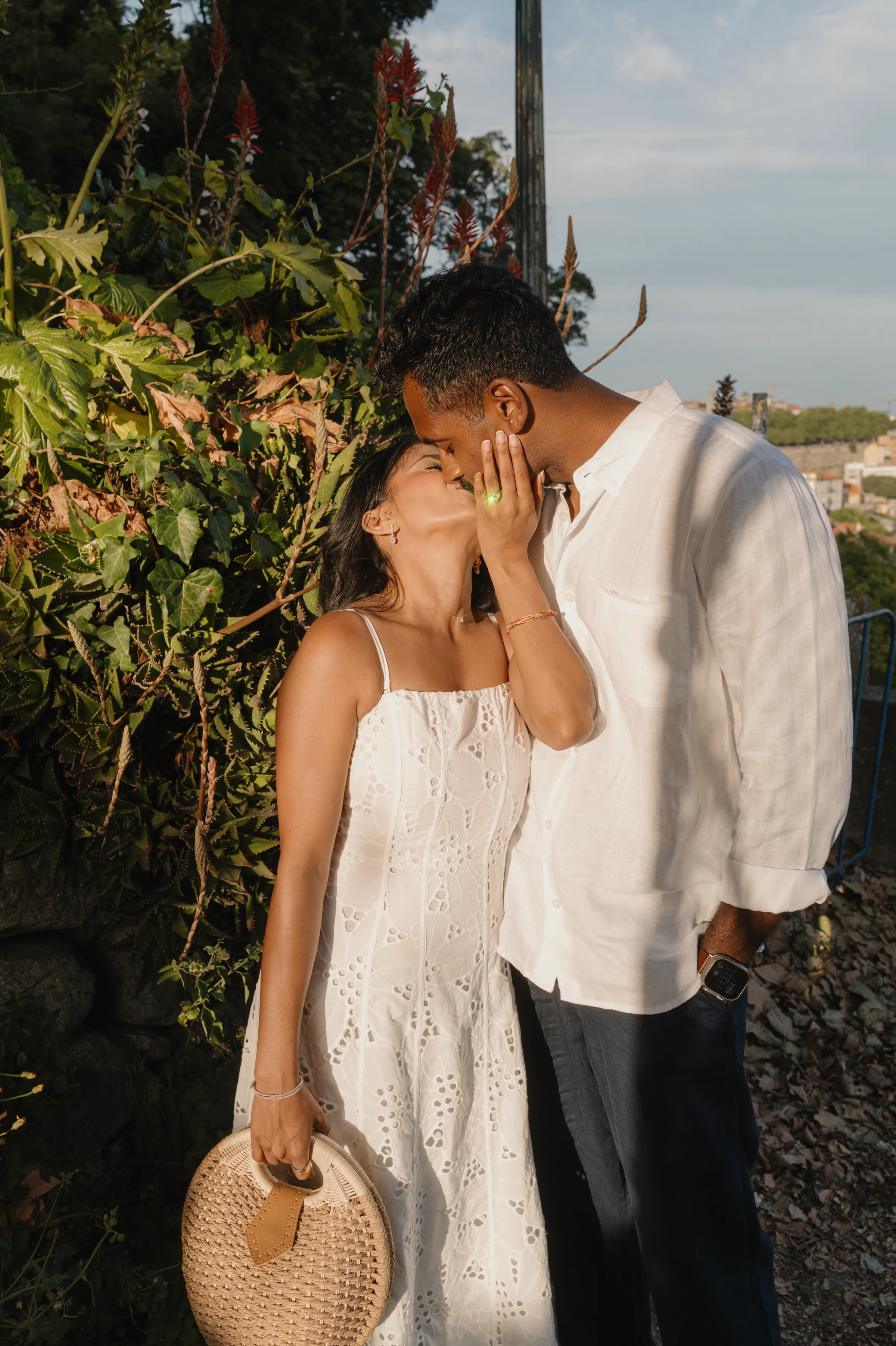 Couple kissing in soft light beside lush garden plants during an outdoor session.
