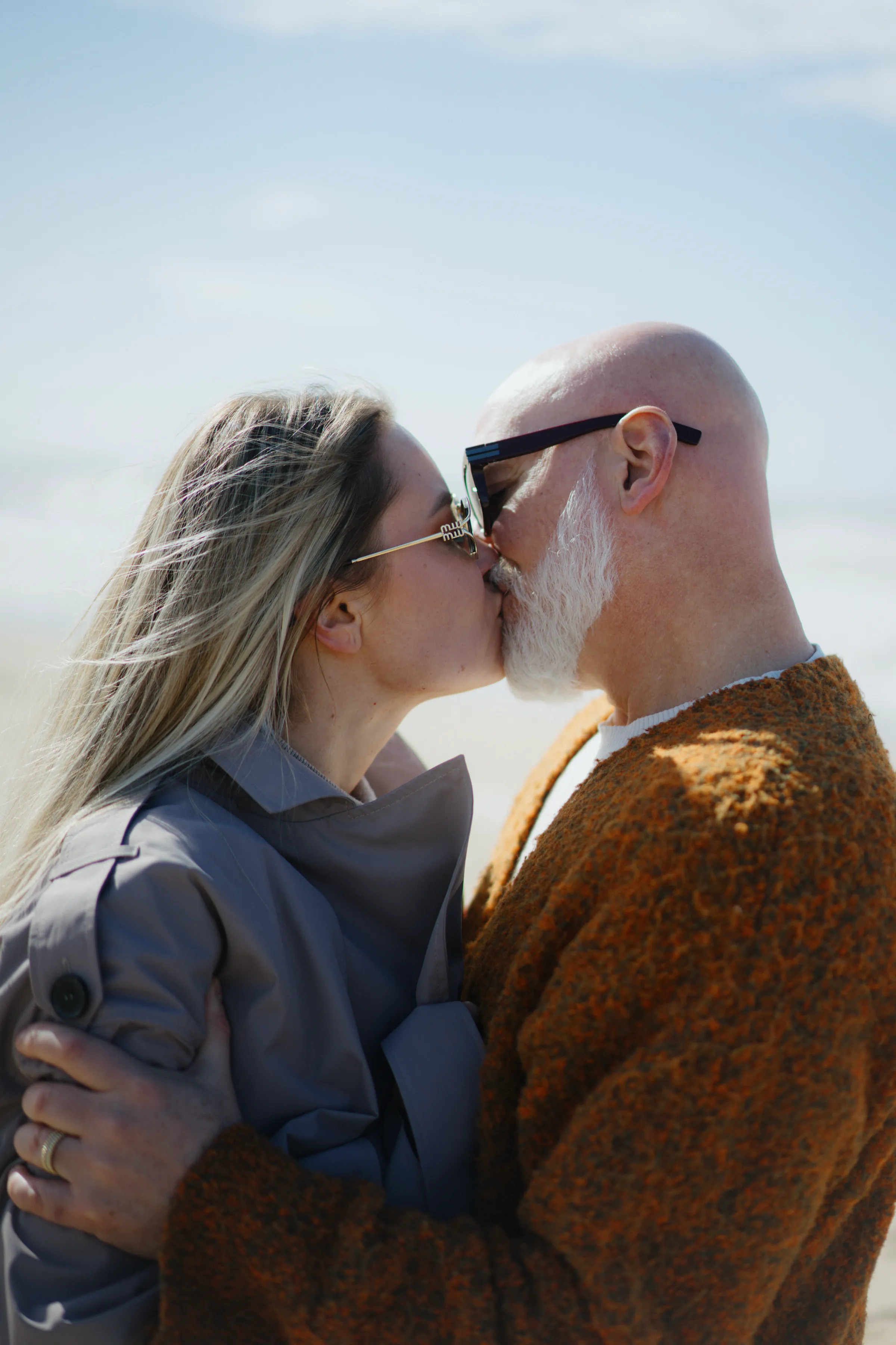 Close outdoor portrait of a couple kissing in soft light against a pale sky.