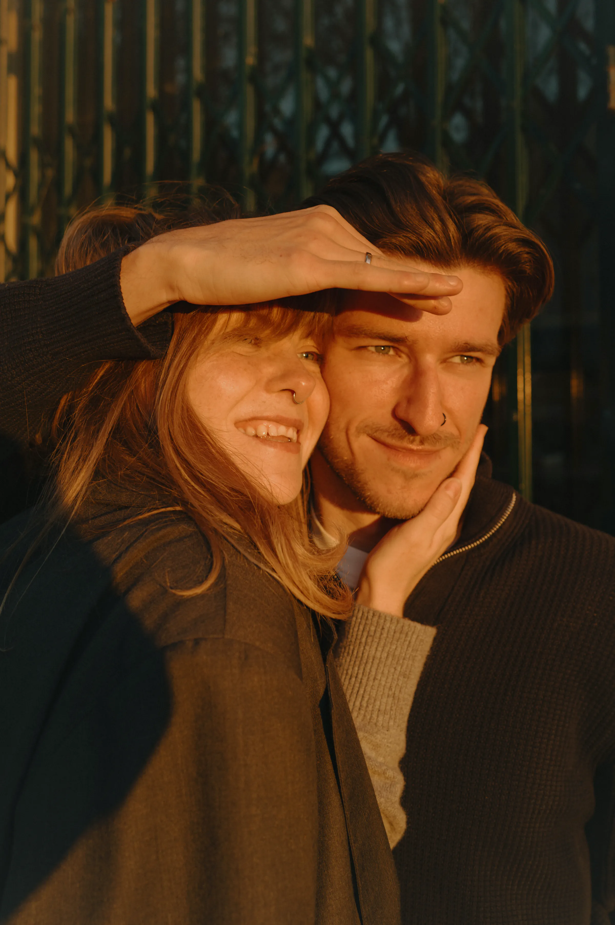 Couple close portrait in warm sunlight, one shading their faces with a hand during an outdoor session.