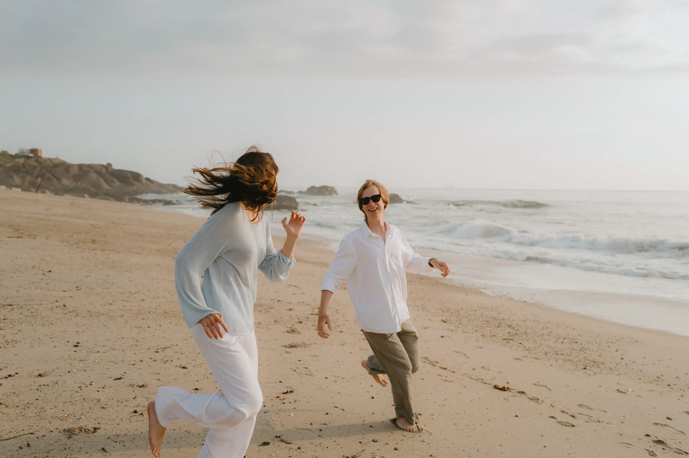 Couple running barefoot on a sandy beach during a relaxed seaside outdoor session.