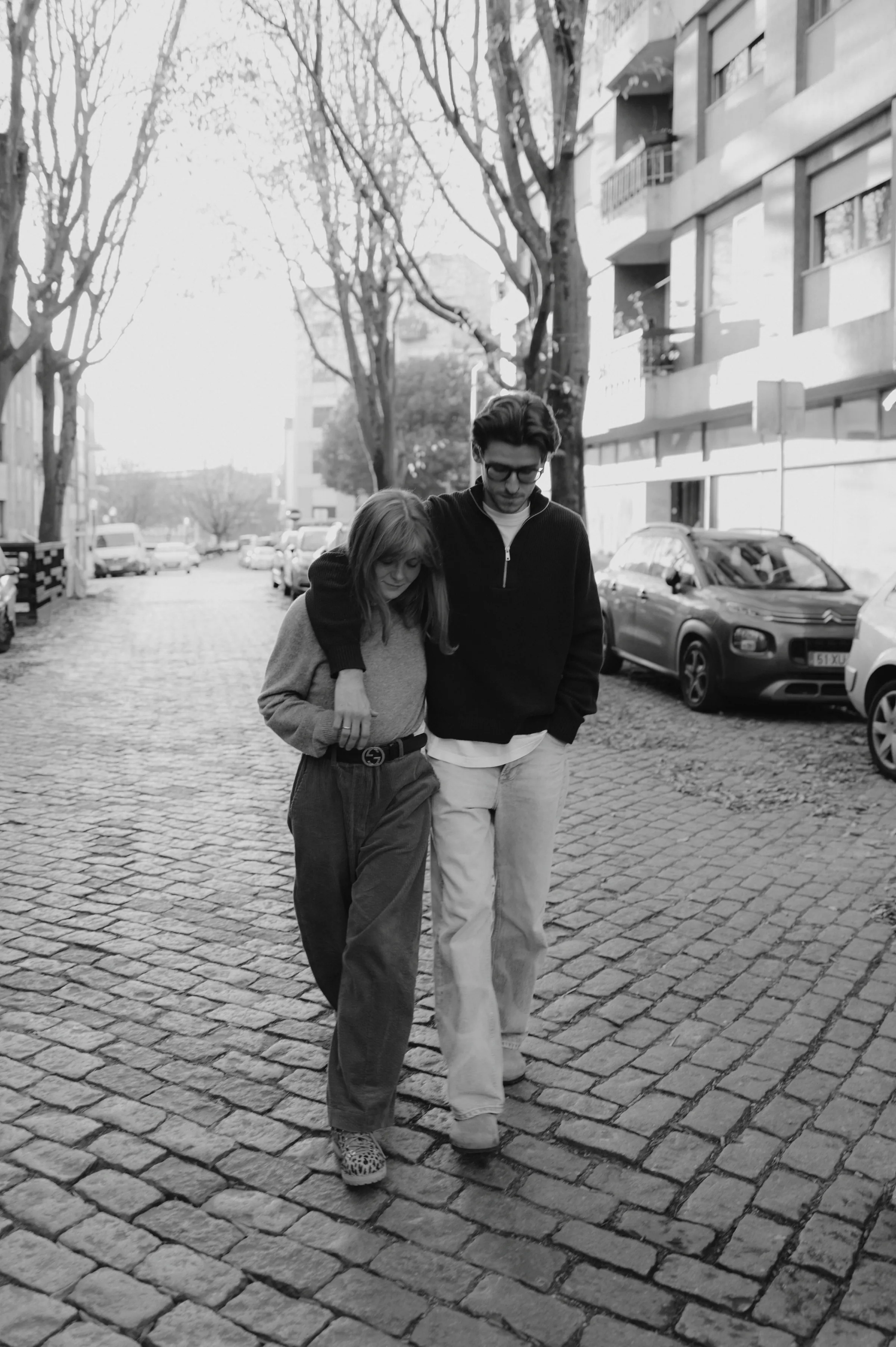 Couple walking closely during a black-and-white city walk on a cobblestone street.