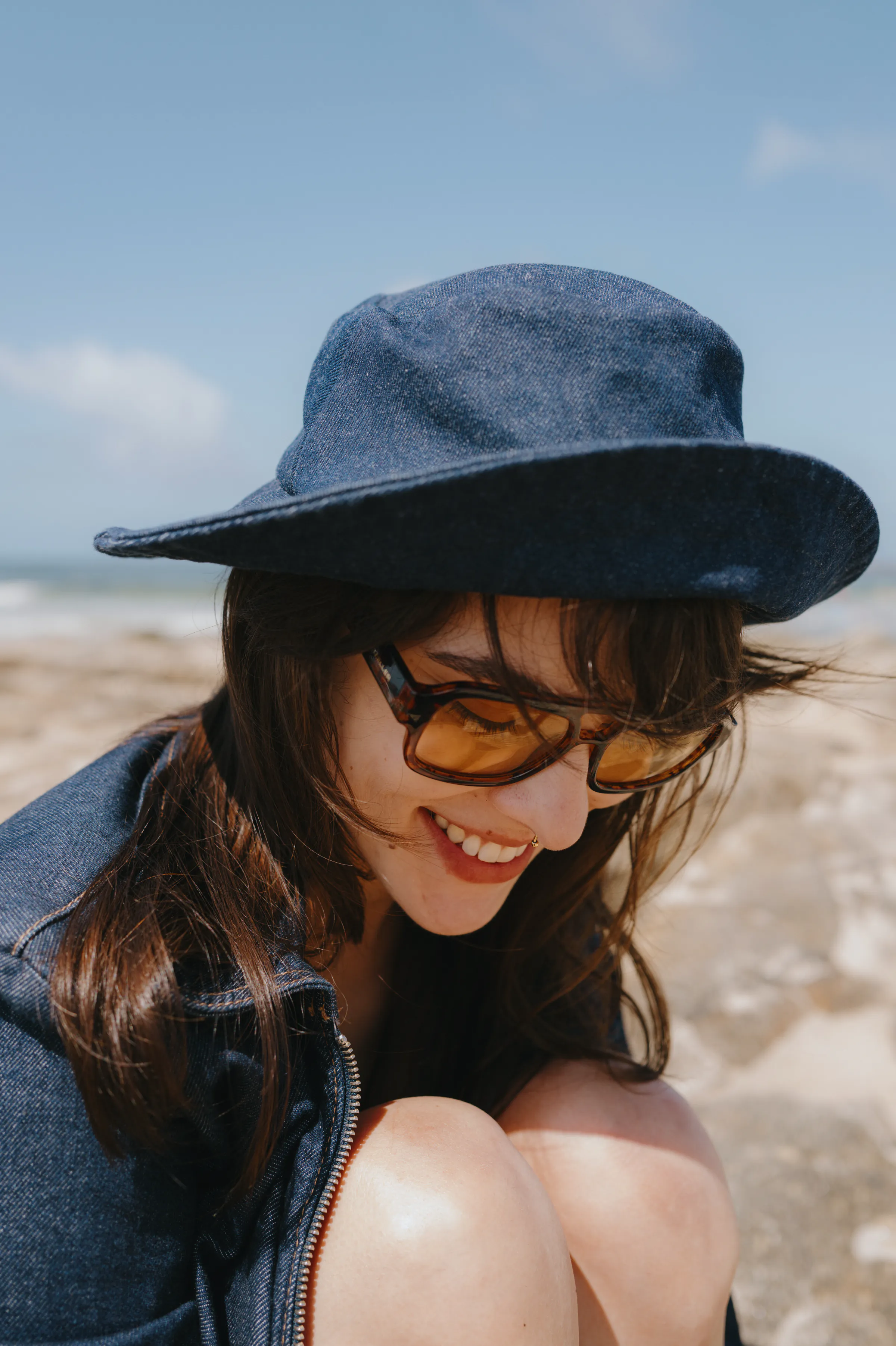 Close portrait of a person in sunglasses and a dark hat during a seaside outdoor session.