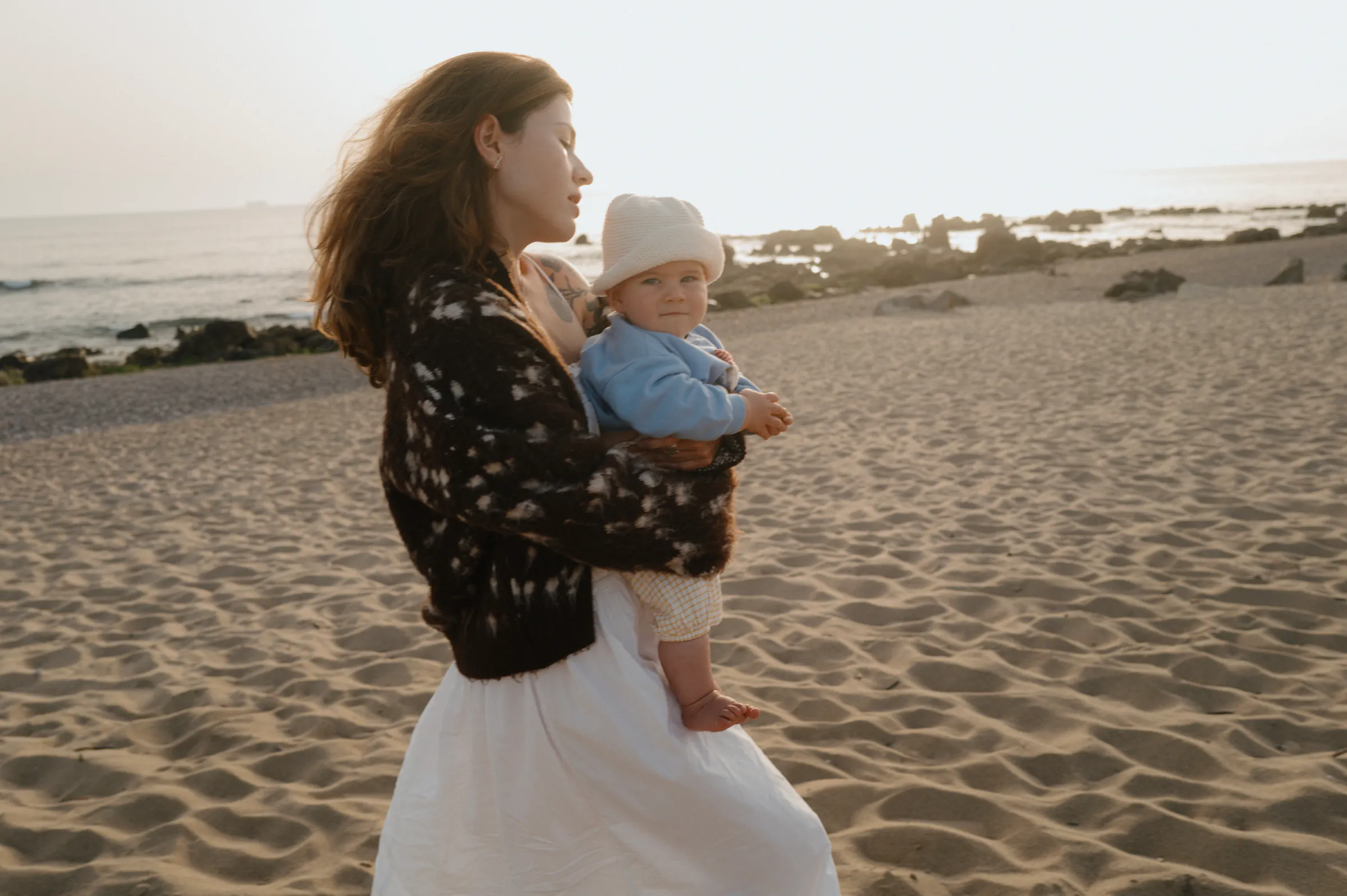Adult holding a baby during a soft light seaside outdoor session on sandy shore.