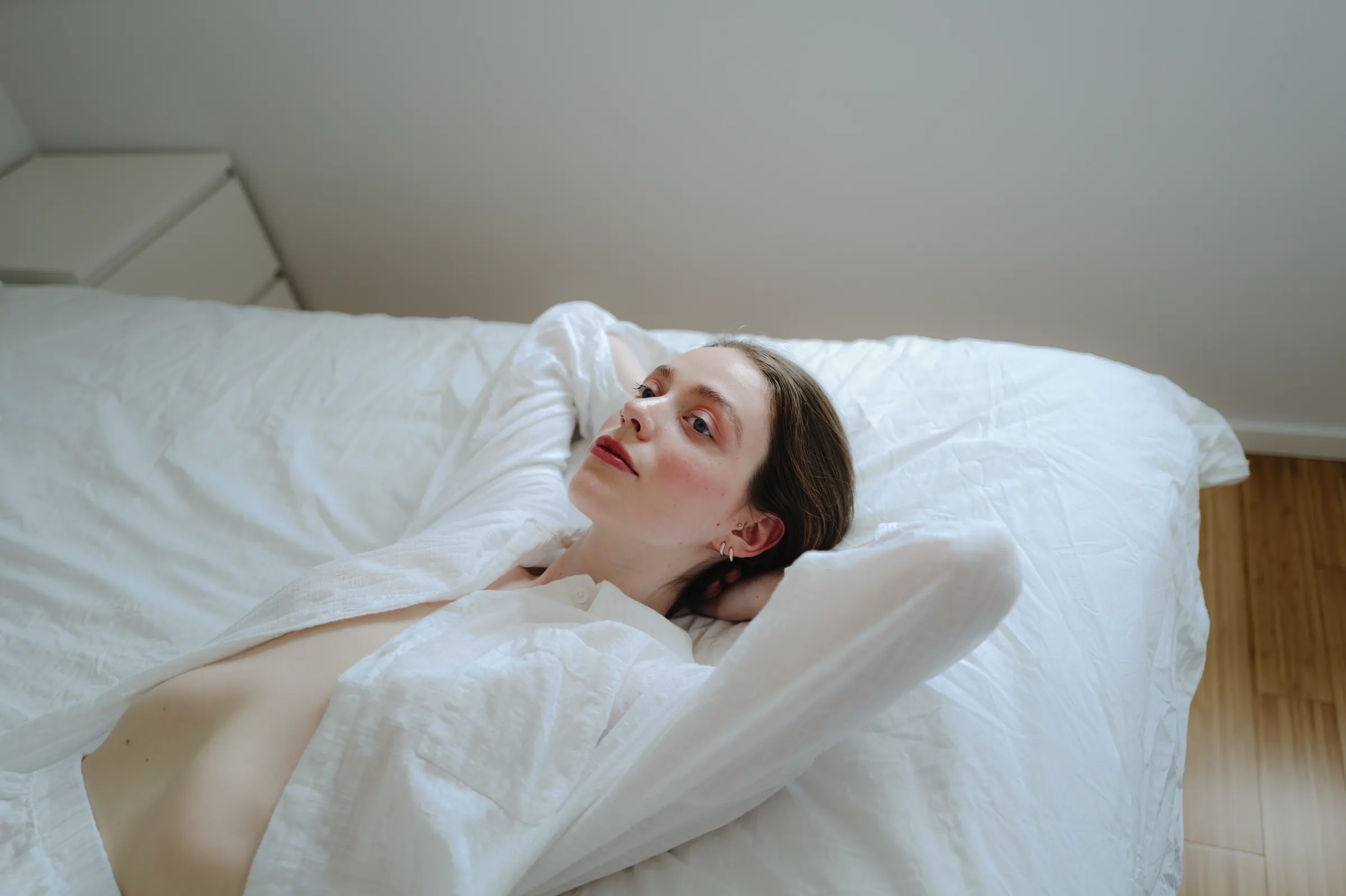 Close portrait of an adult reclining on a white bed during a soft light home session.