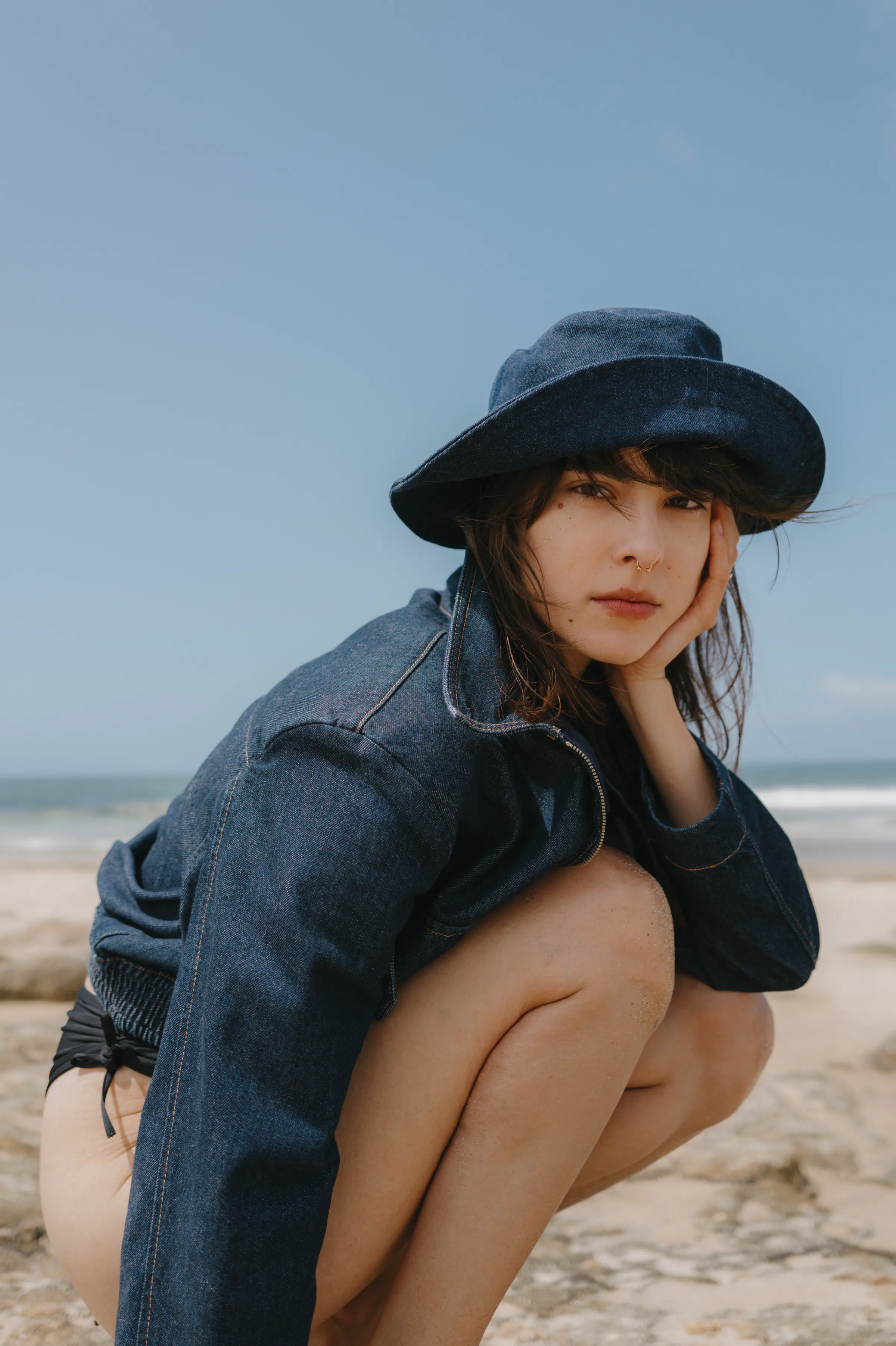 Close portrait on a sandy seaside, with a dark hat, denim jacket, and soft coastal light.
