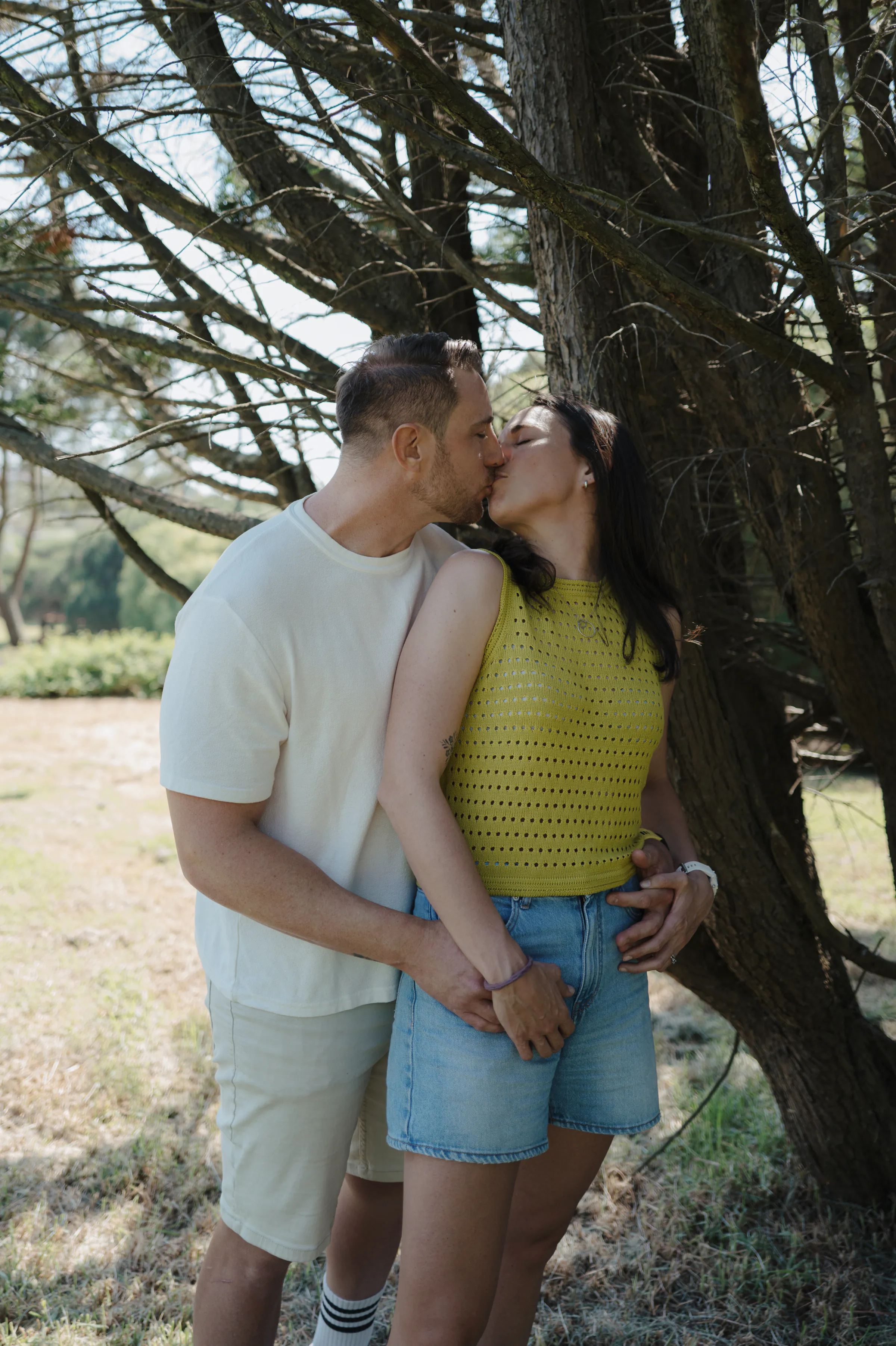 Couple sharing a kiss beneath a tree during a soft light outdoor session.