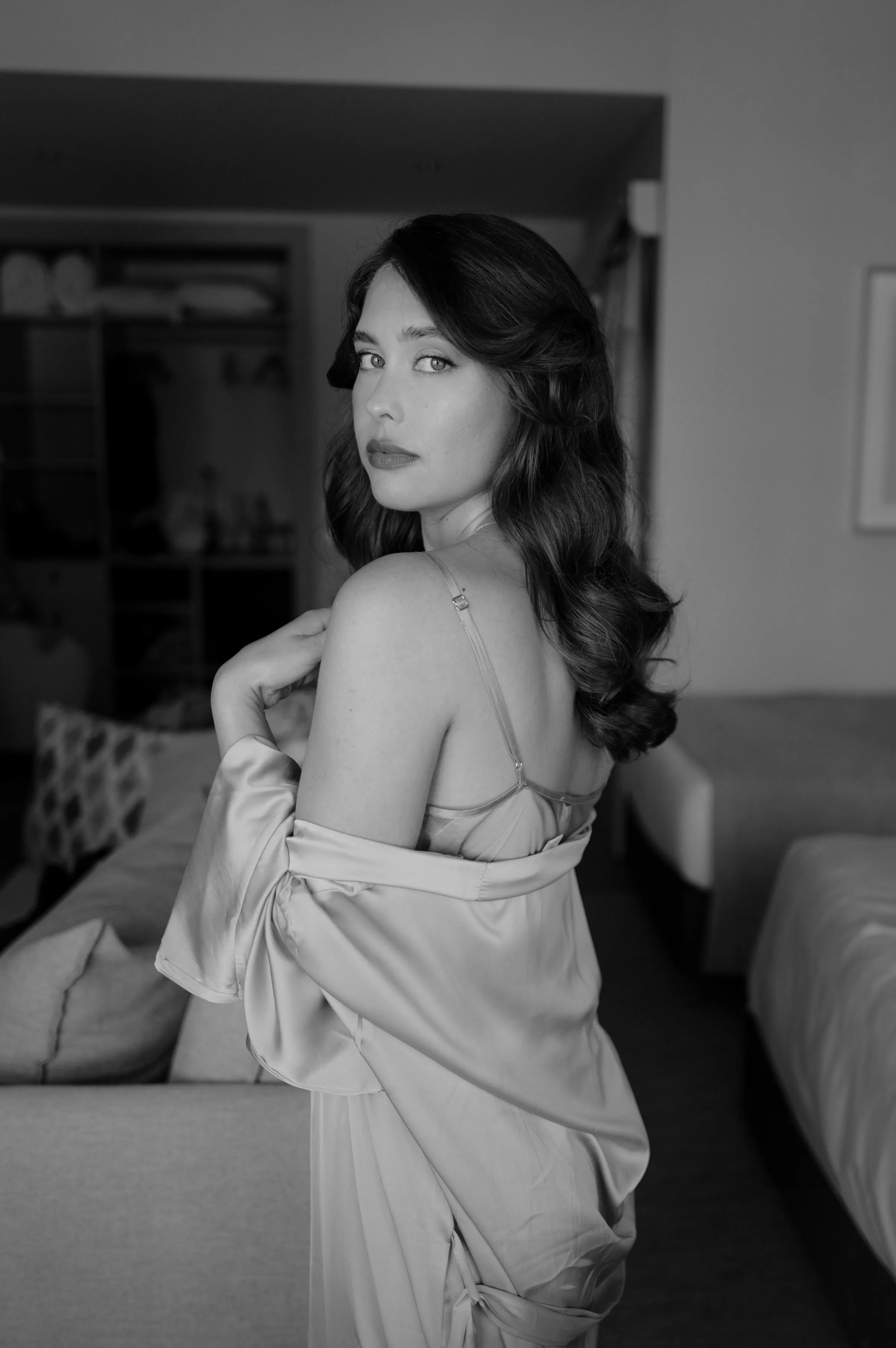 Black-and-white home session portrait of a woman looking over her shoulder in soft indoor light.