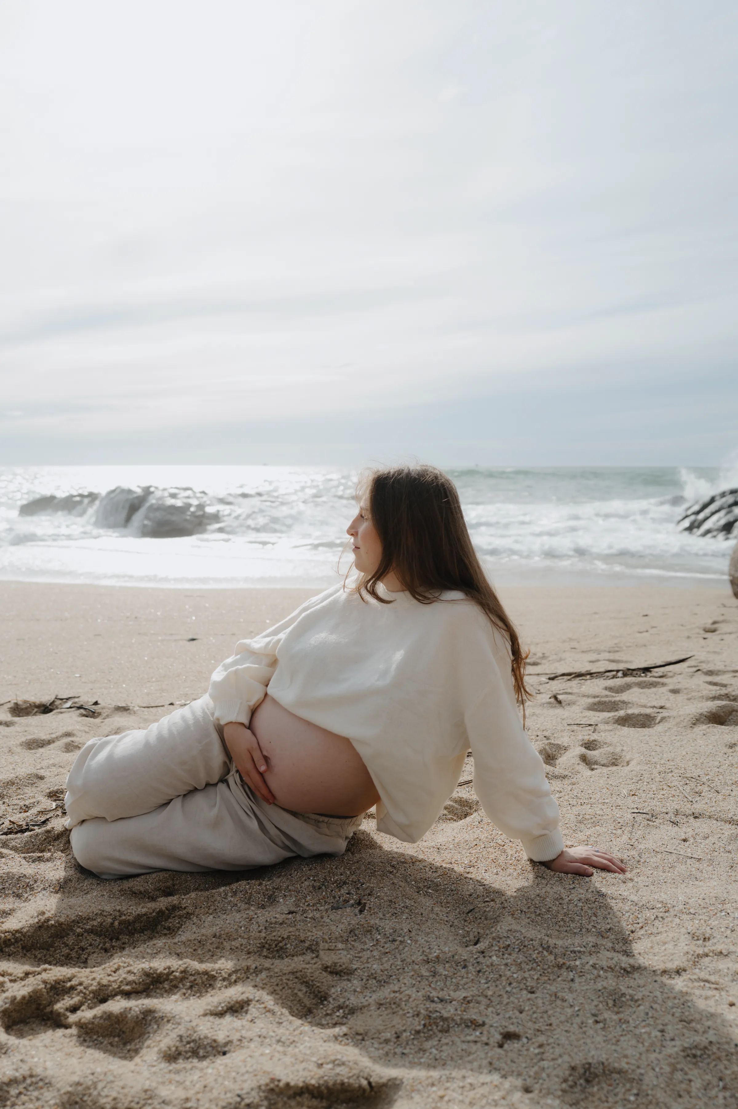 Person reclining on sandy beach beside gentle waves during a soft light seaside portrait.