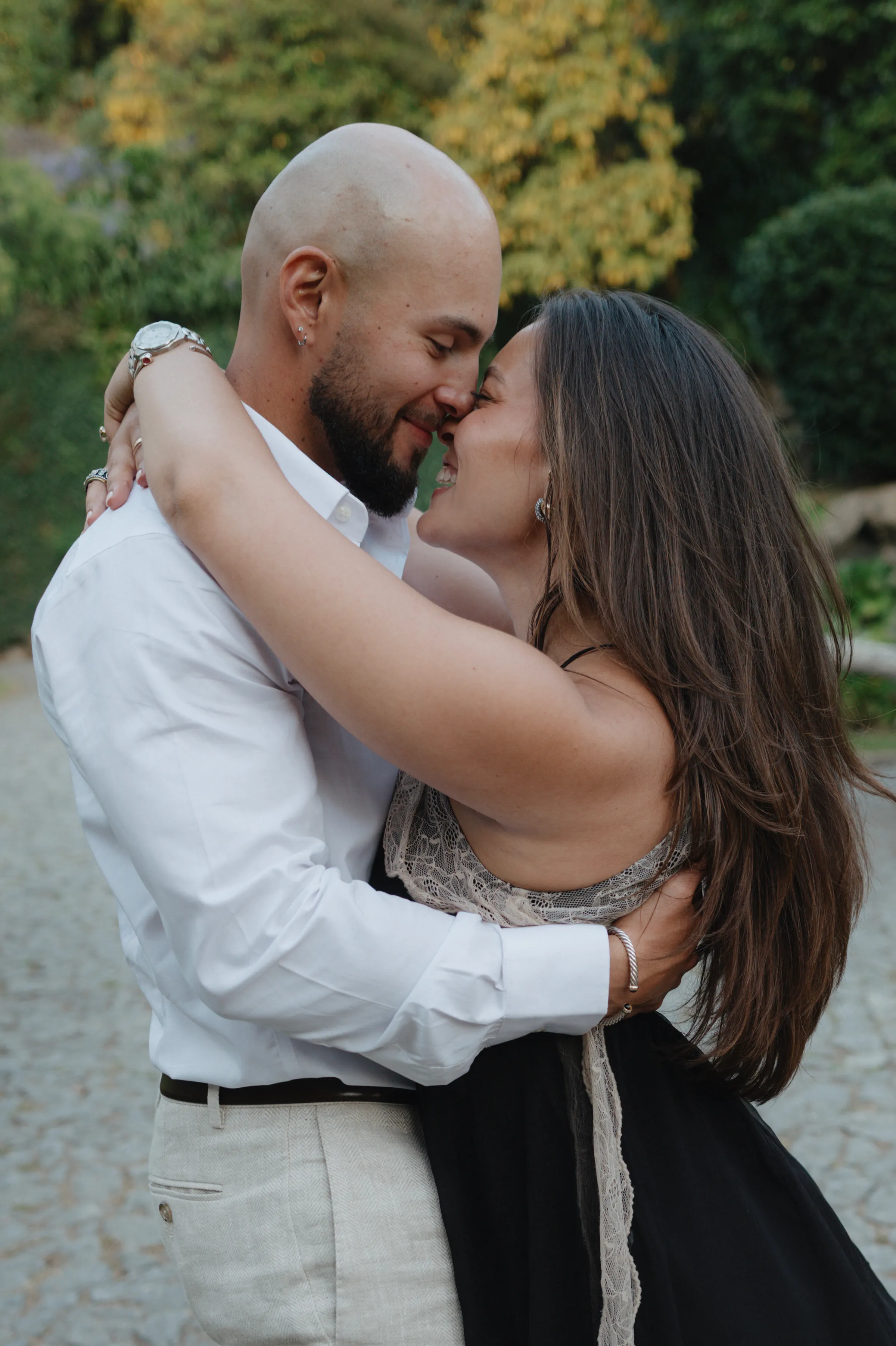 Couple embracing on a cobblestone garden path during an outdoor session in soft light.