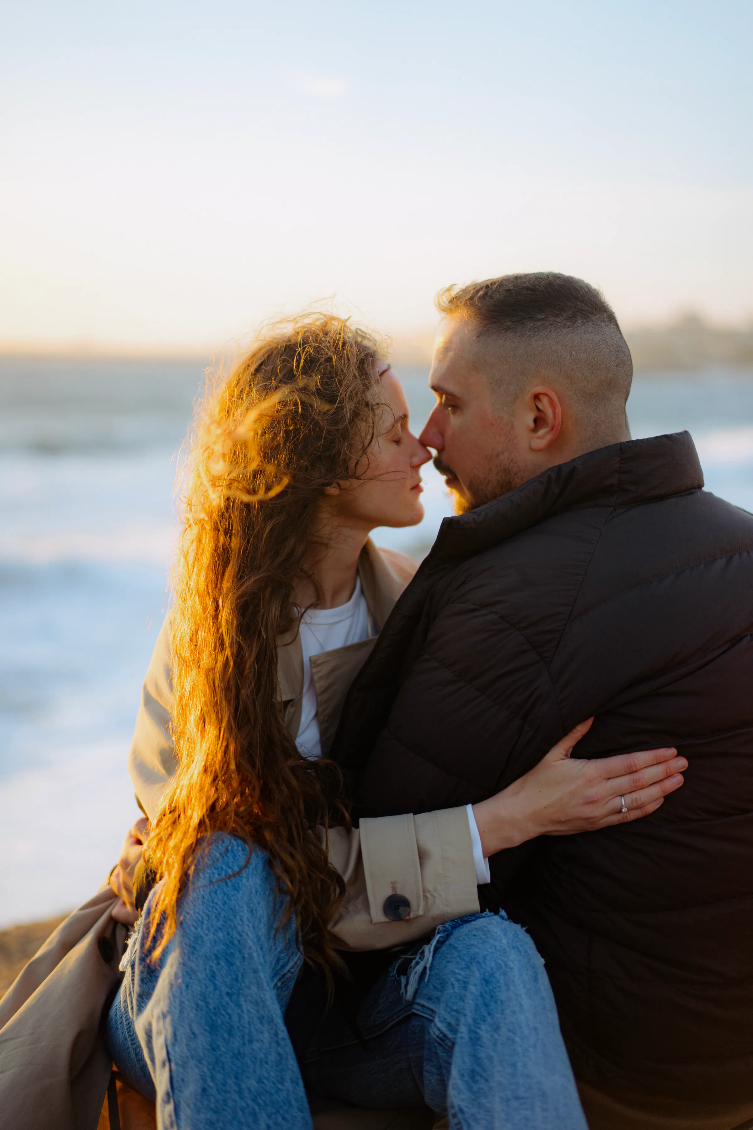 Couple sharing a close kiss during a seaside outdoor session in soft evening light.