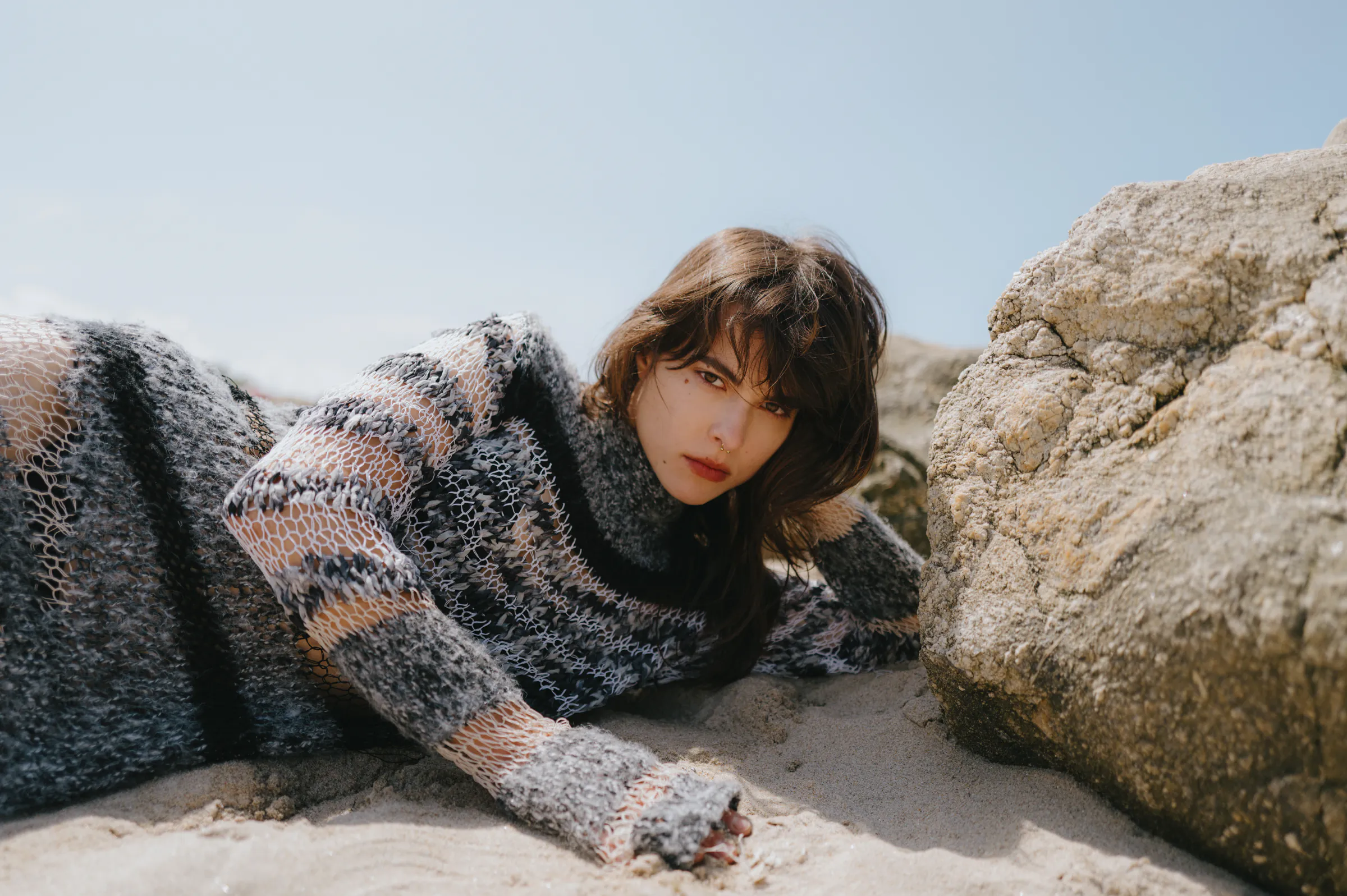 Close portrait of a person reclining on sand beside coastal rocks in soft outdoor light