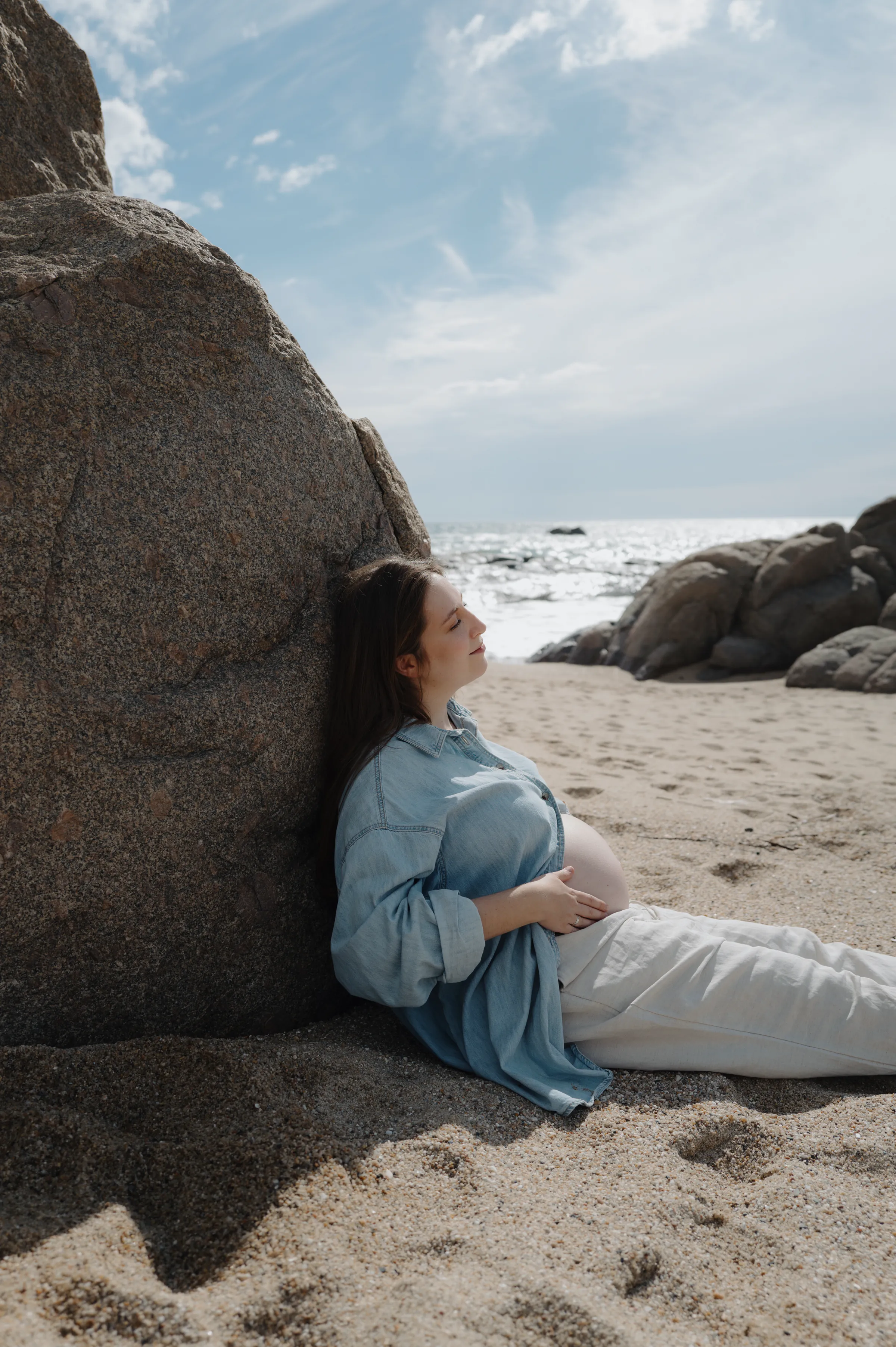 Seaside portrait of a person reclining against a large rock on sandy beach in soft light