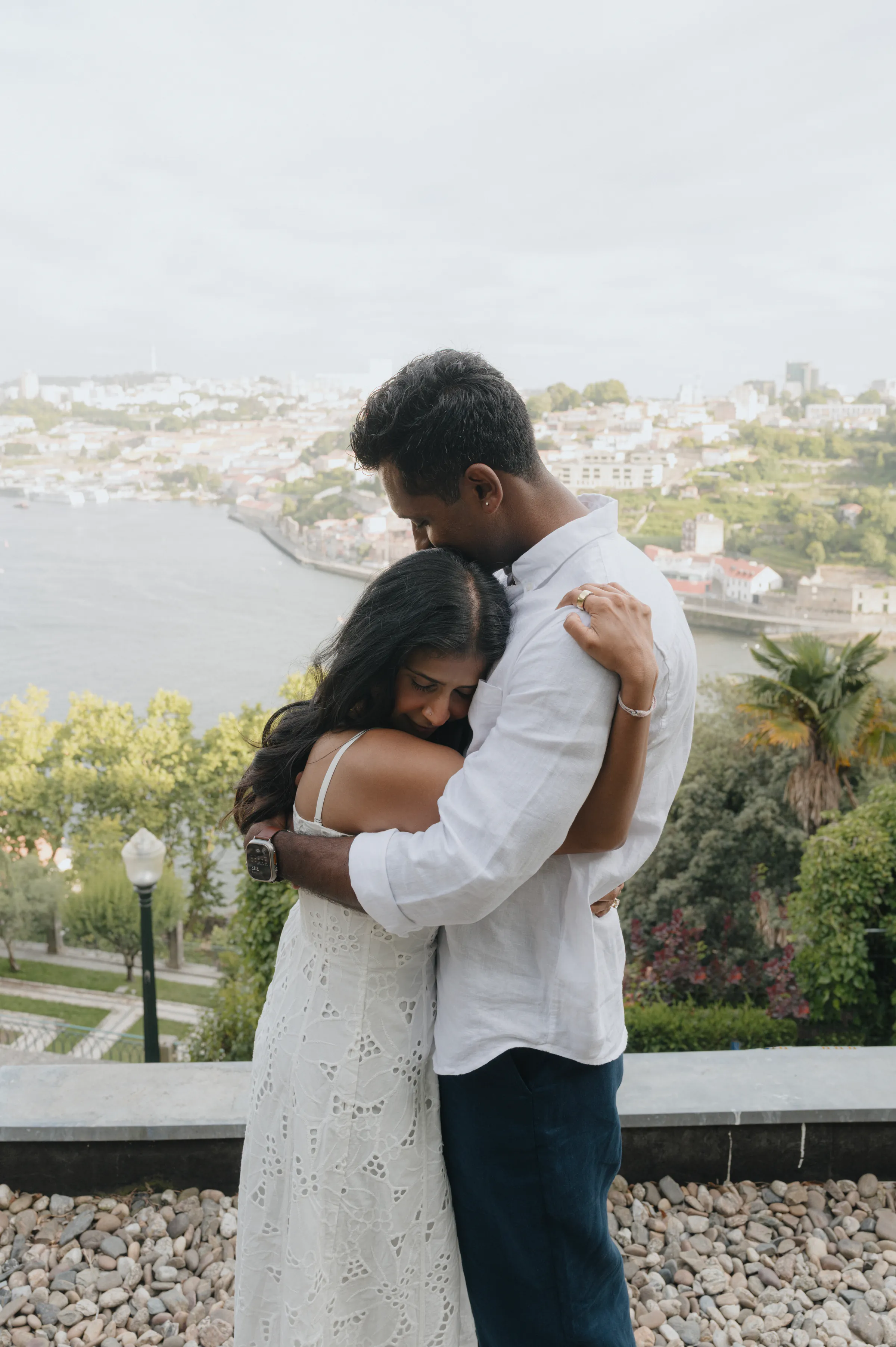 Couple embracing during an outdoor session overlooking a river and city in soft light