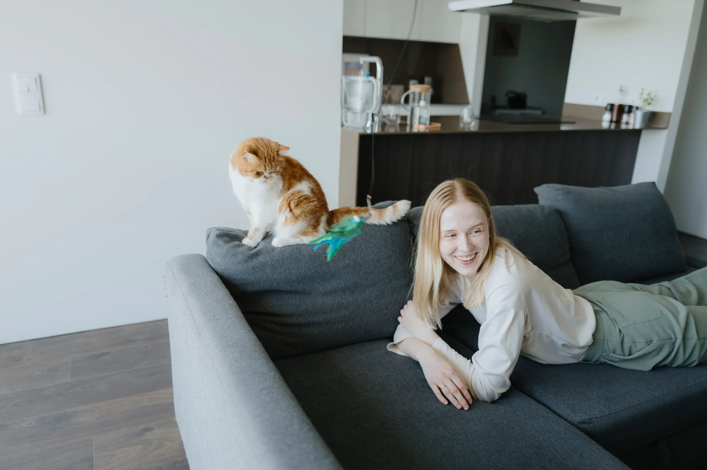 Home session portrait of a person reclining on a gray sofa beside an orange-and-white cat.