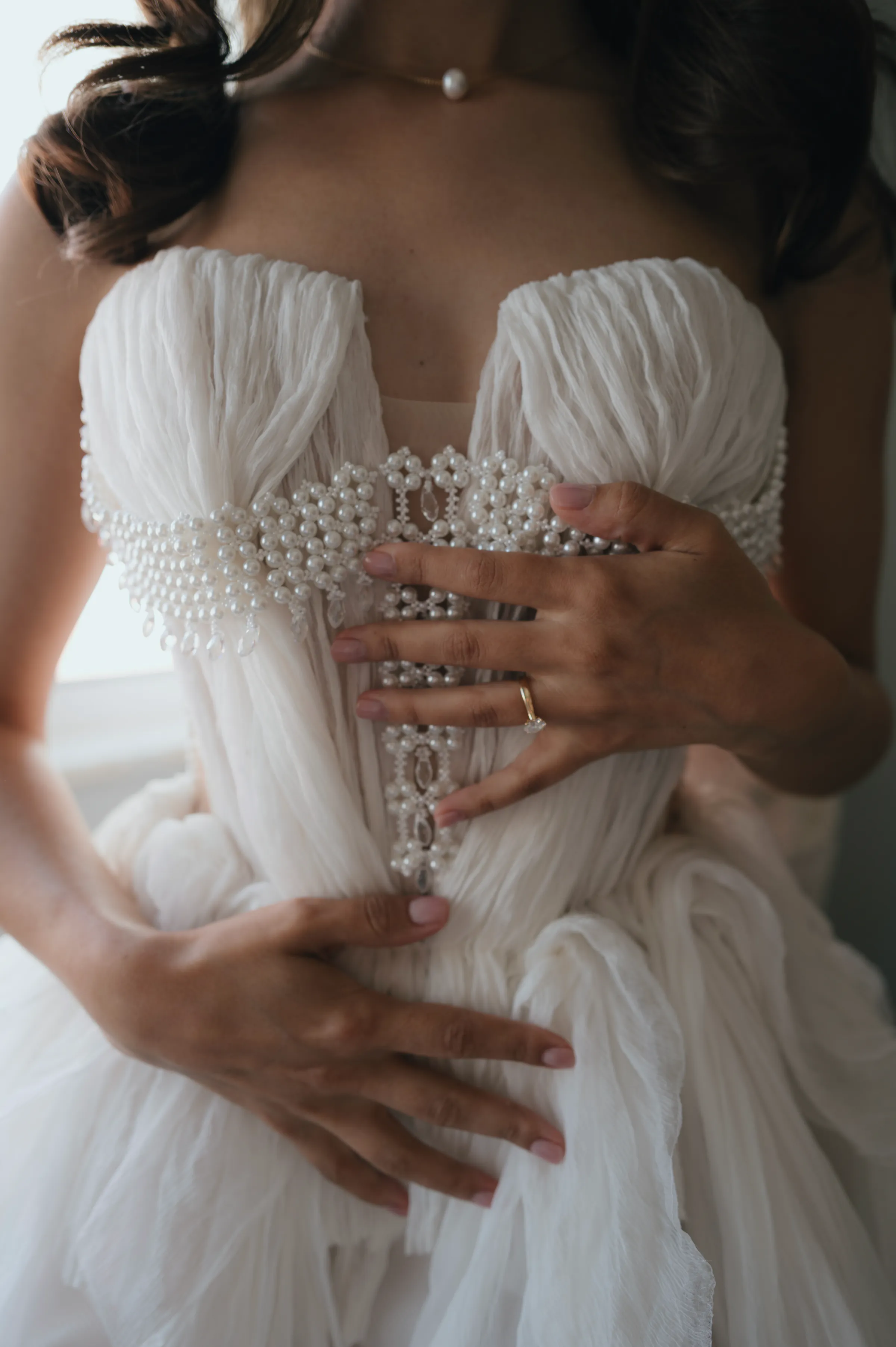 Close portrait detail of a person in a white beaded gown, hands resting on soft tulle.