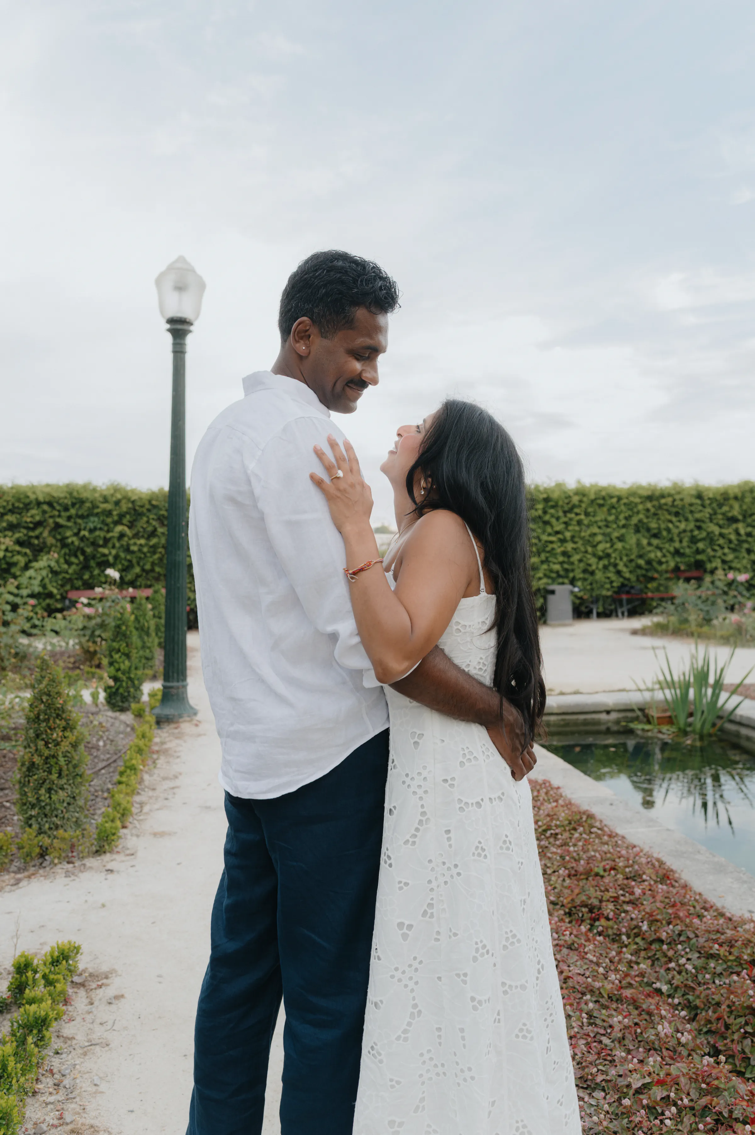 Couple portrait in a garden by a pond, standing close together in soft overcast light.