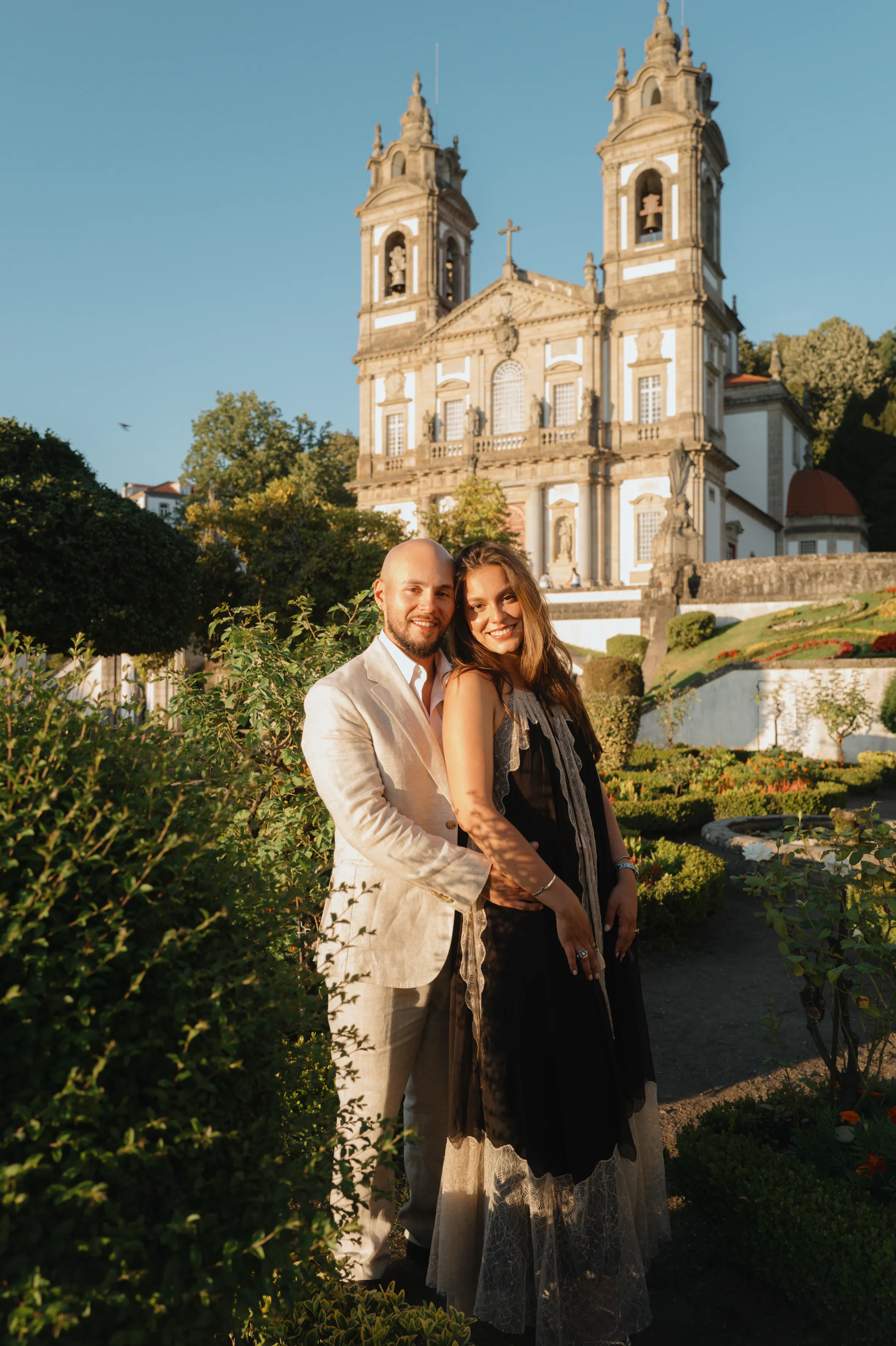 Couple portrait in a garden with an ornate church backdrop during a warm outdoor session.