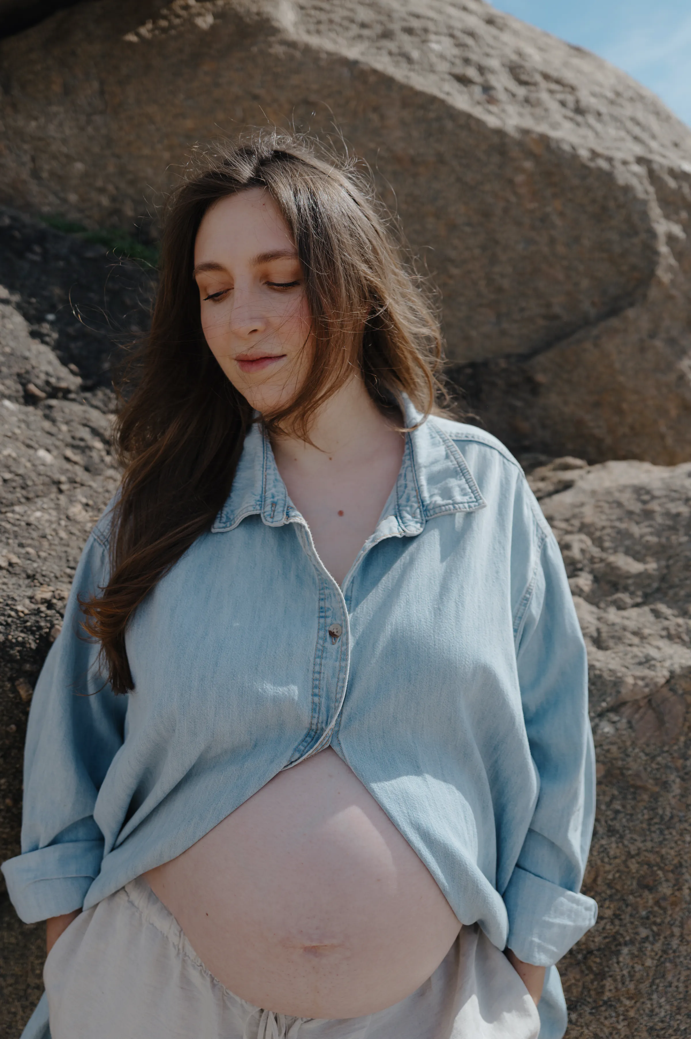 Outdoor portrait of a person in a denim shirt standing among sunlit rocks.