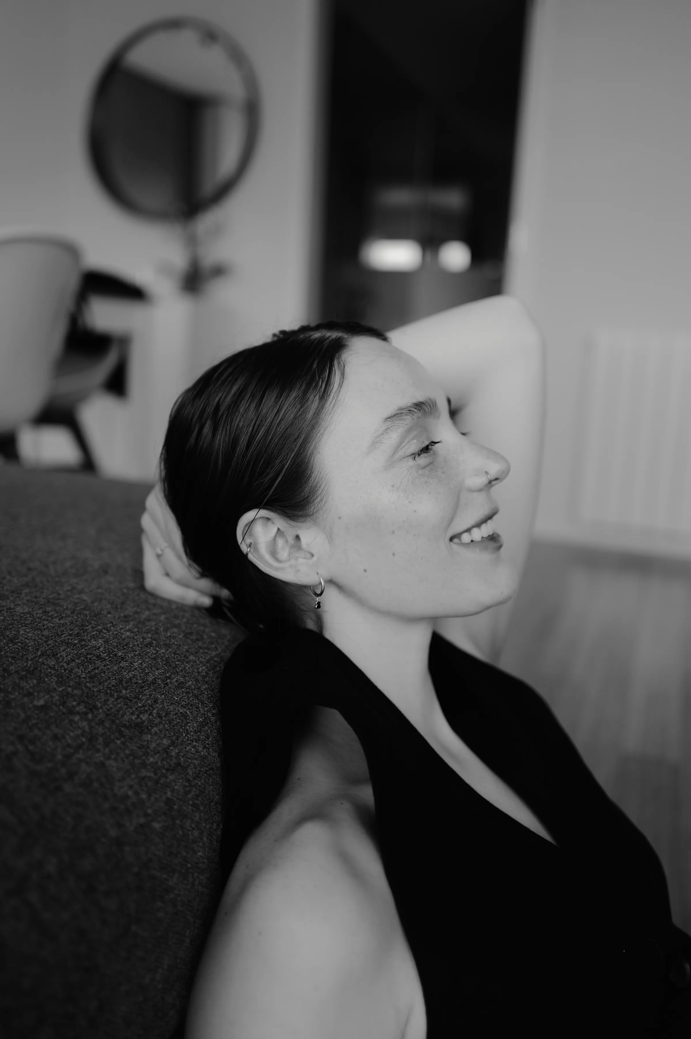 Black-and-white close portrait of a person reclining on a sofa in soft indoor light.