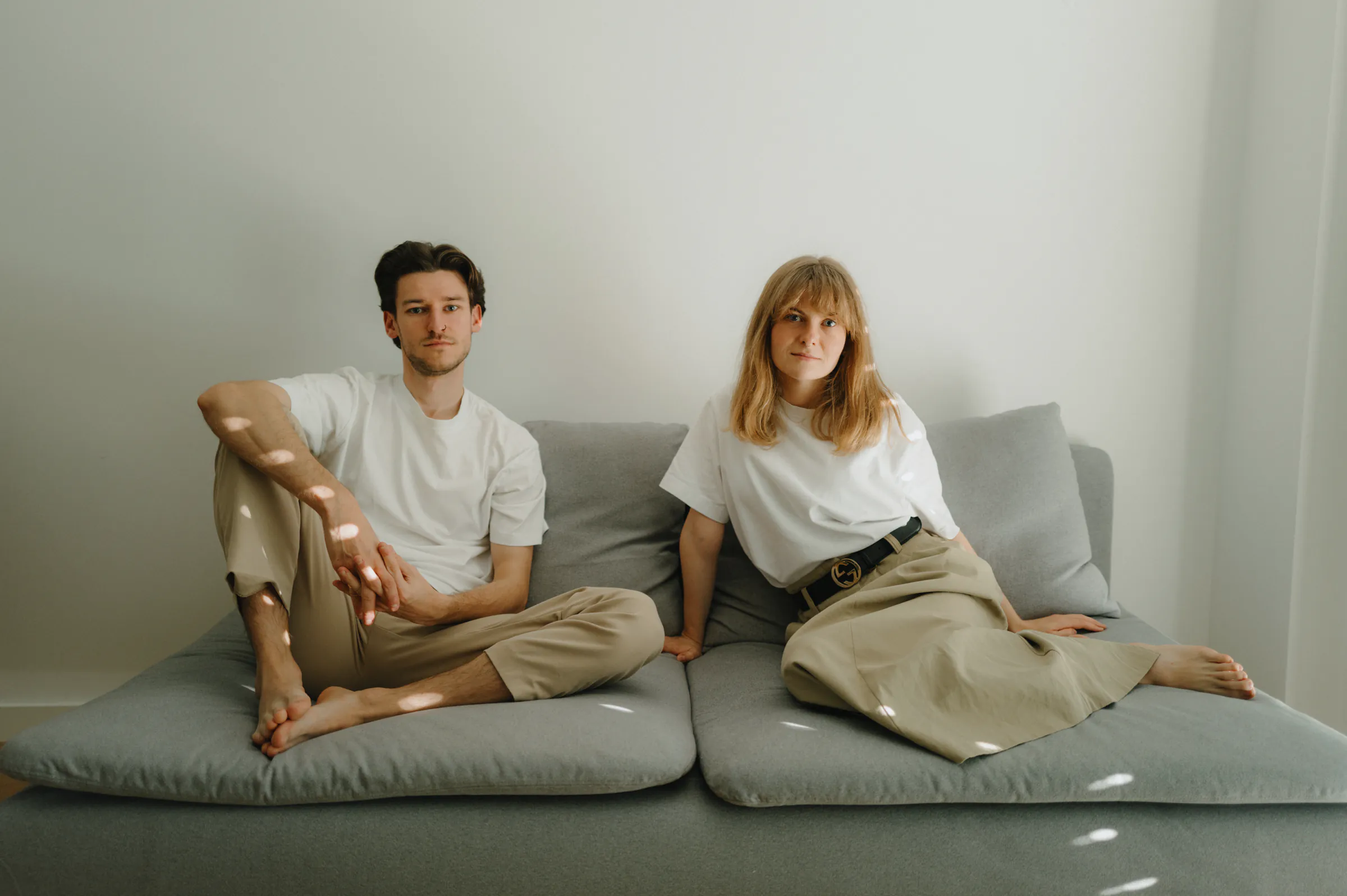 Couple portrait on a low gray sofa during a minimal home session in soft light.