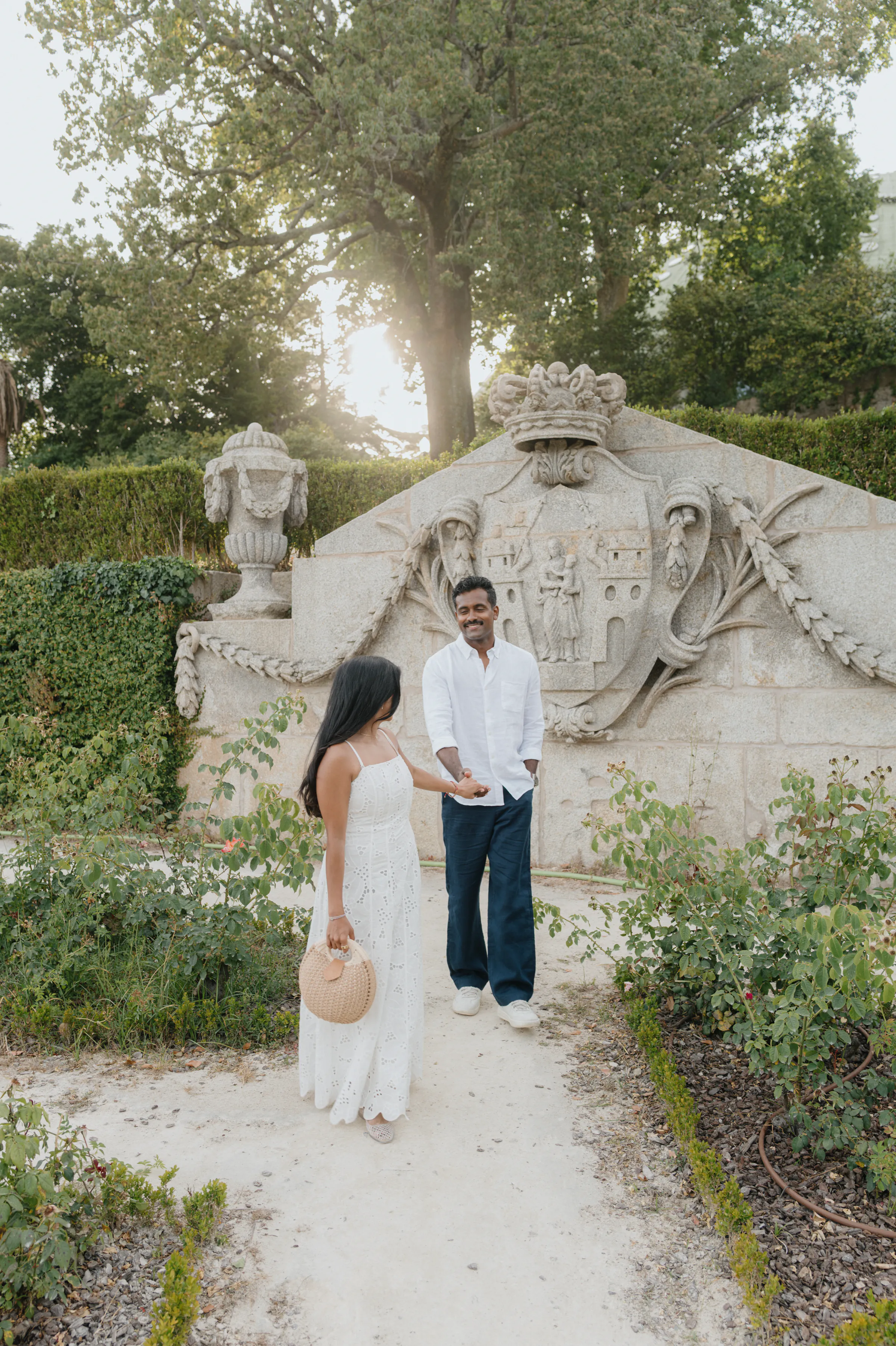 Couple portrait on a garden path beside an ornate stone wall in soft light.