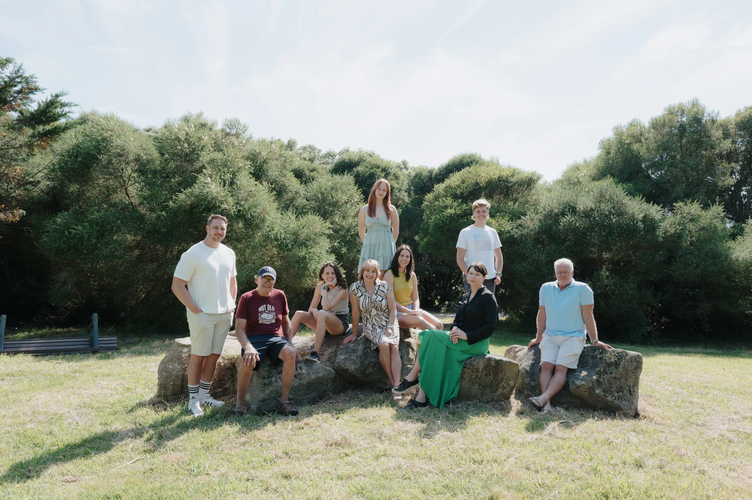Group portrait during an outdoor session, adults and a child gathered on rocks in a sunny park.