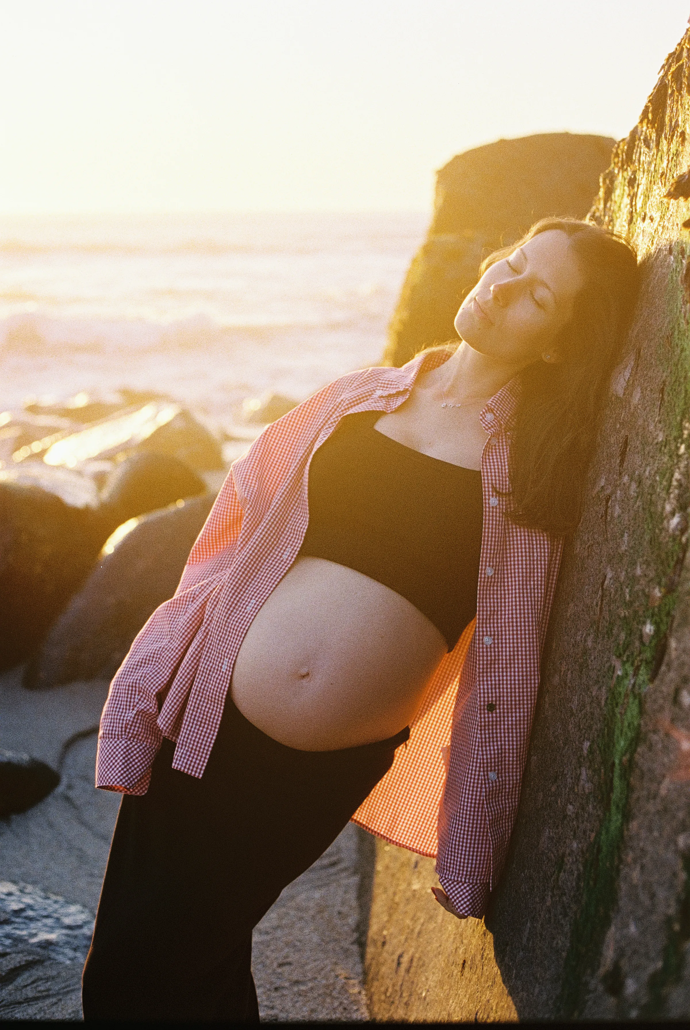 Seaside portrait of a person leaning against rocks in warm soft light.