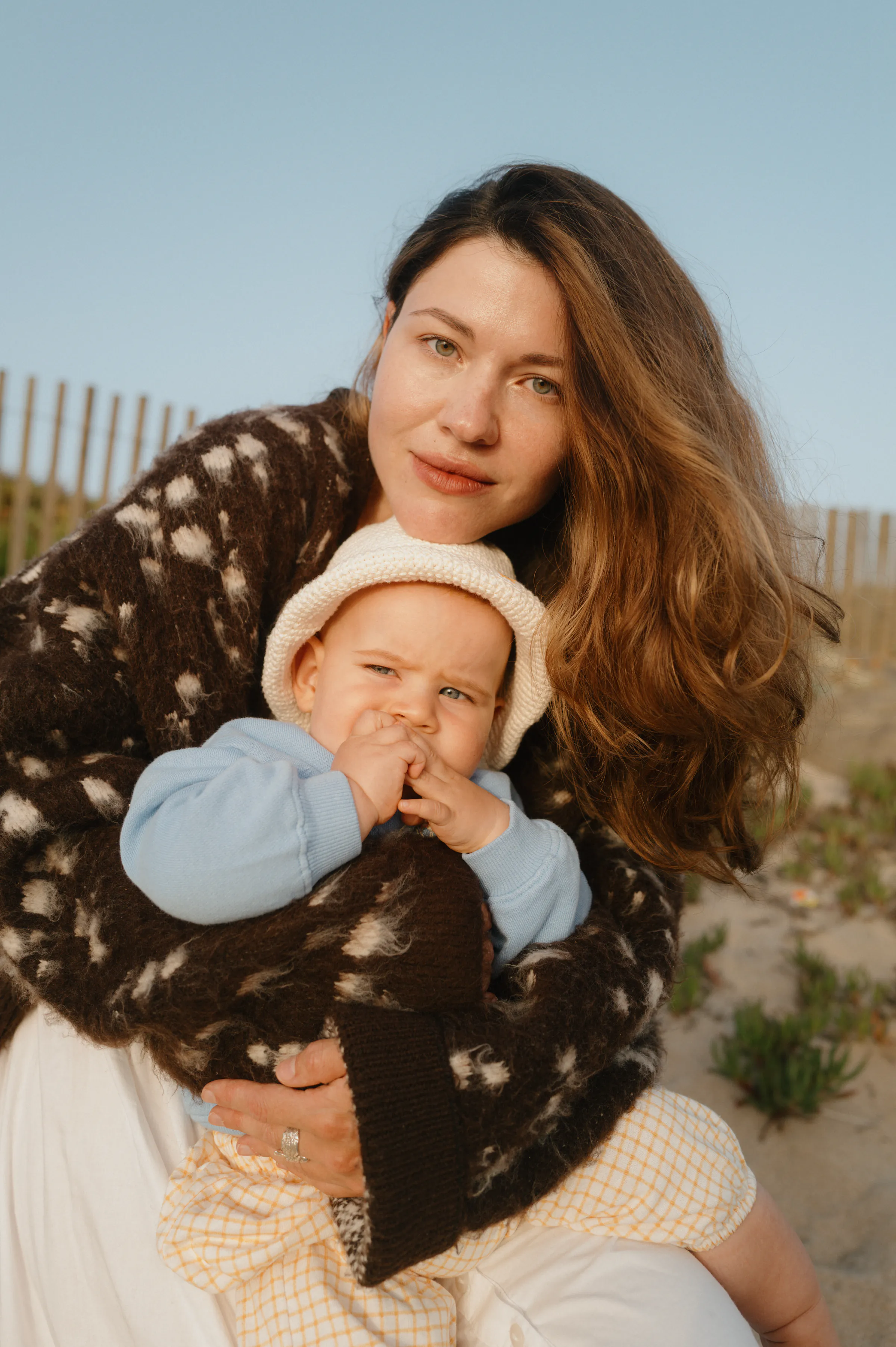 Close outdoor portrait of an adult holding a baby in soft light near a beach fence.
