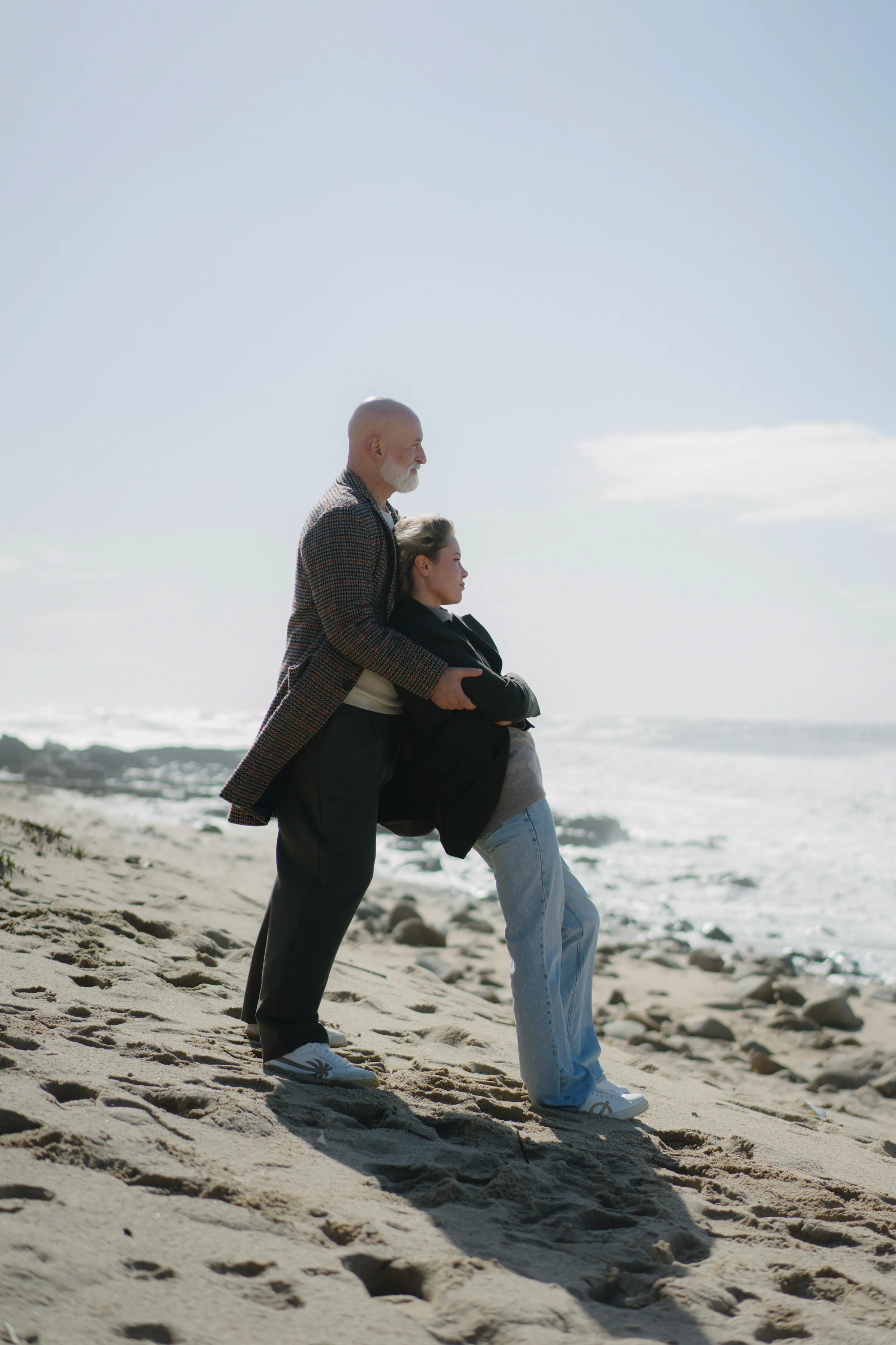Couple standing close together during a seaside session on a sandy beach in soft coastal light.