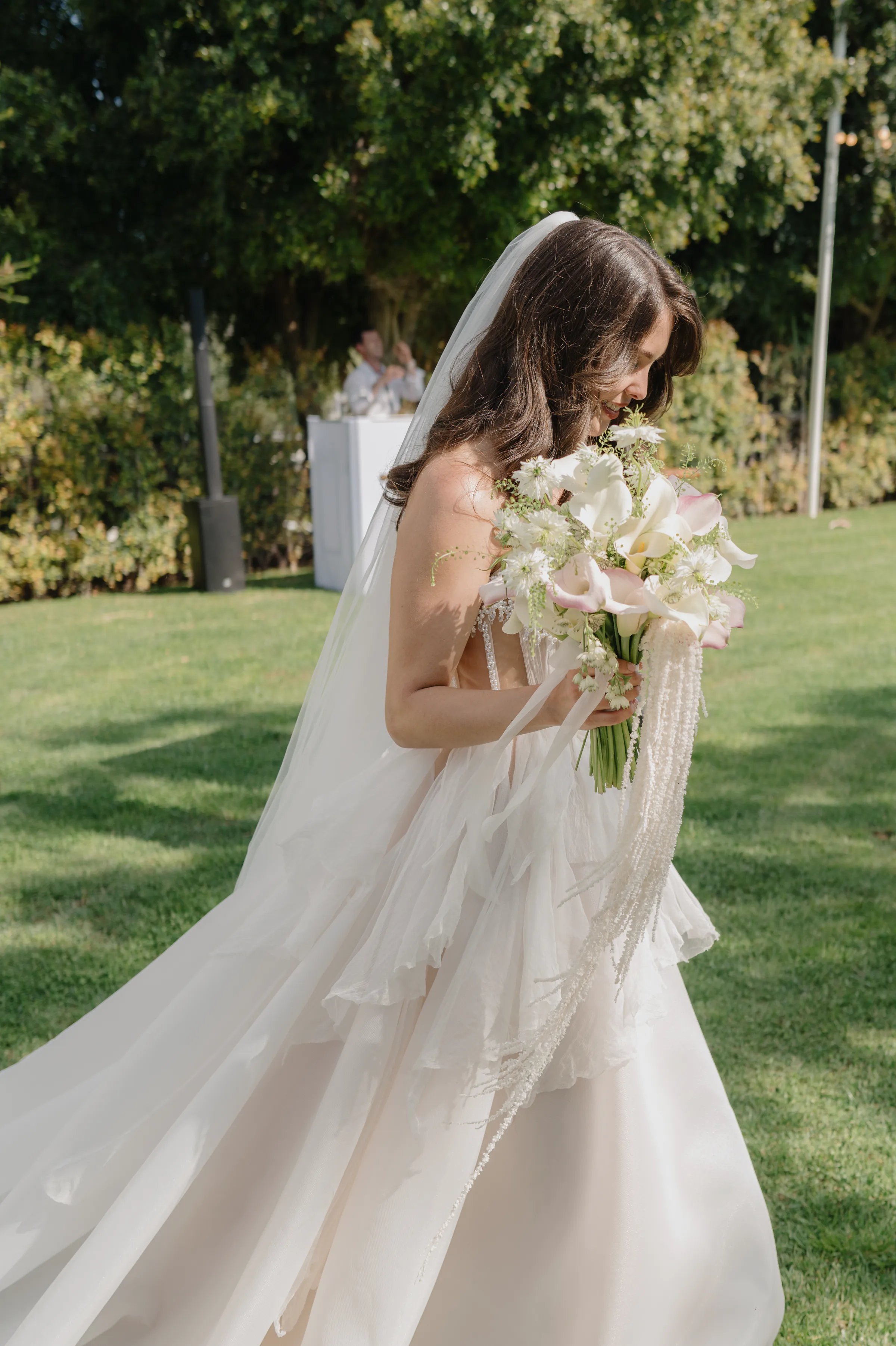 Bride in a veil and gown holding a pale bouquet during a soft light garden portrait.
